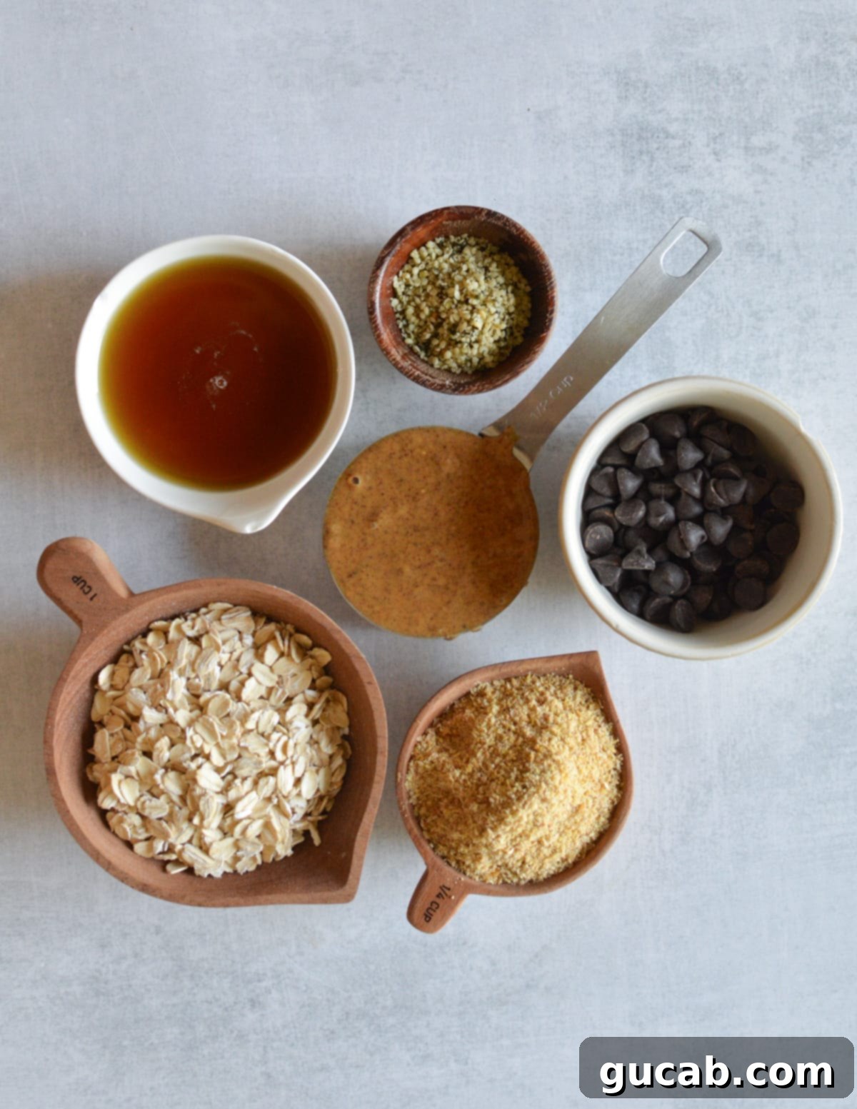 Individual ingredients laid out: almond butter, maple syrup, hemp hearts, golden flax meal, oats, and dark chocolate chips.