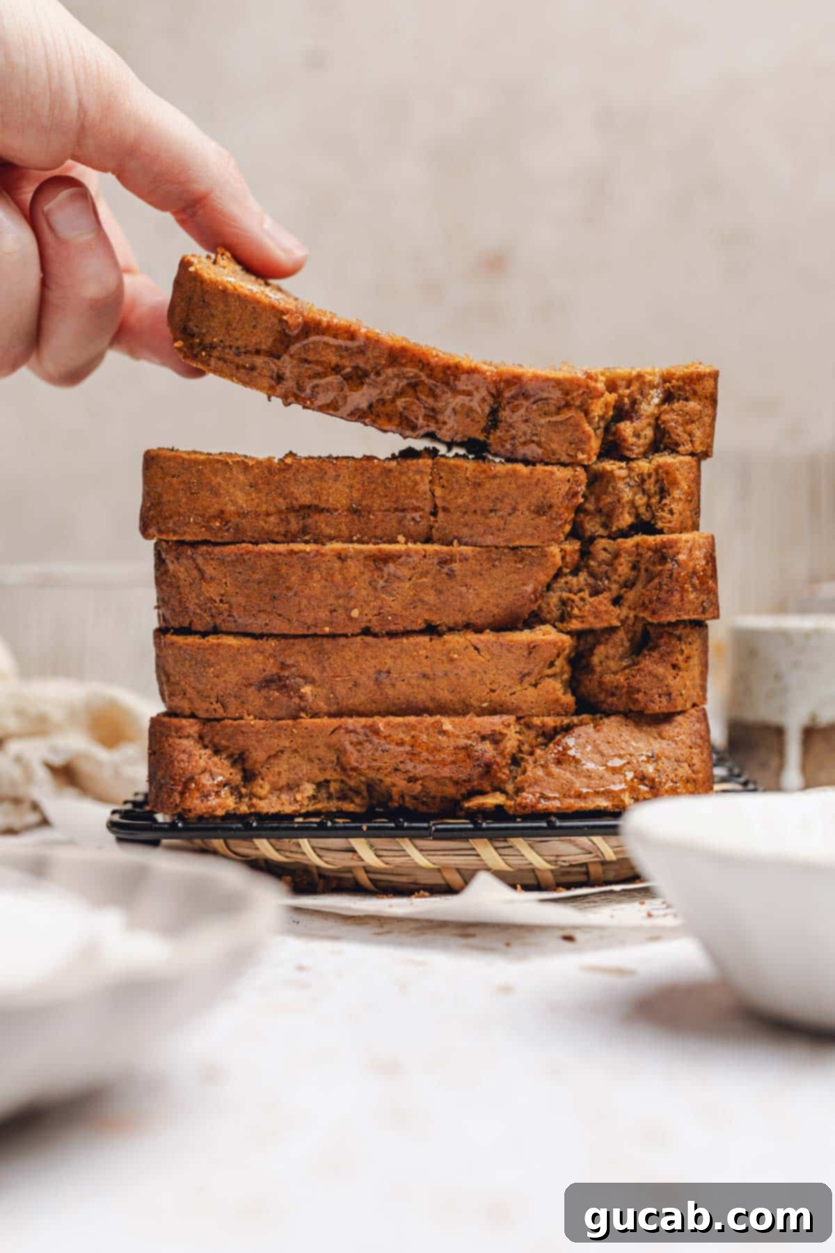 A hand gently placing a fresh slice of honey banana bread onto a growing stack of slices.