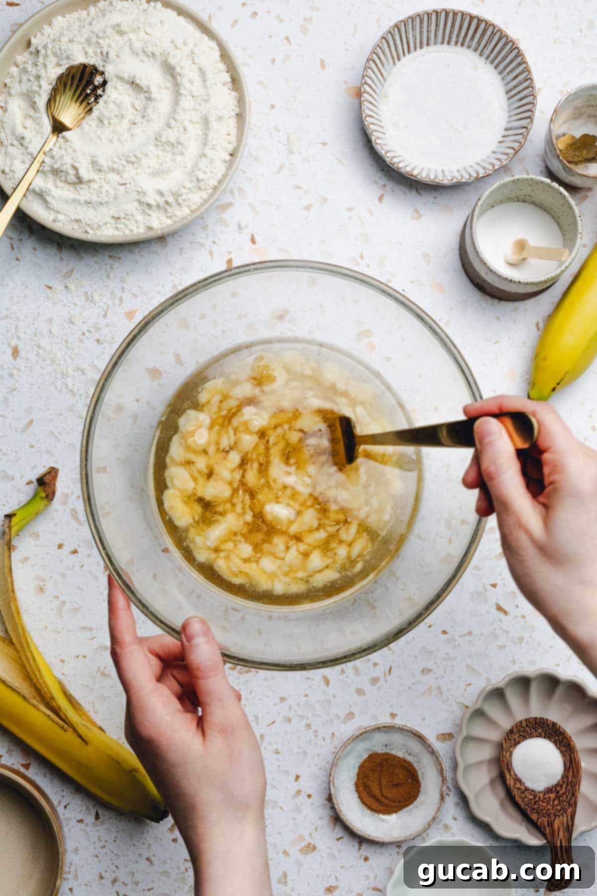 A hand using a fork to mix melted coconut oil, mashed bananas, and honey in a bowl.