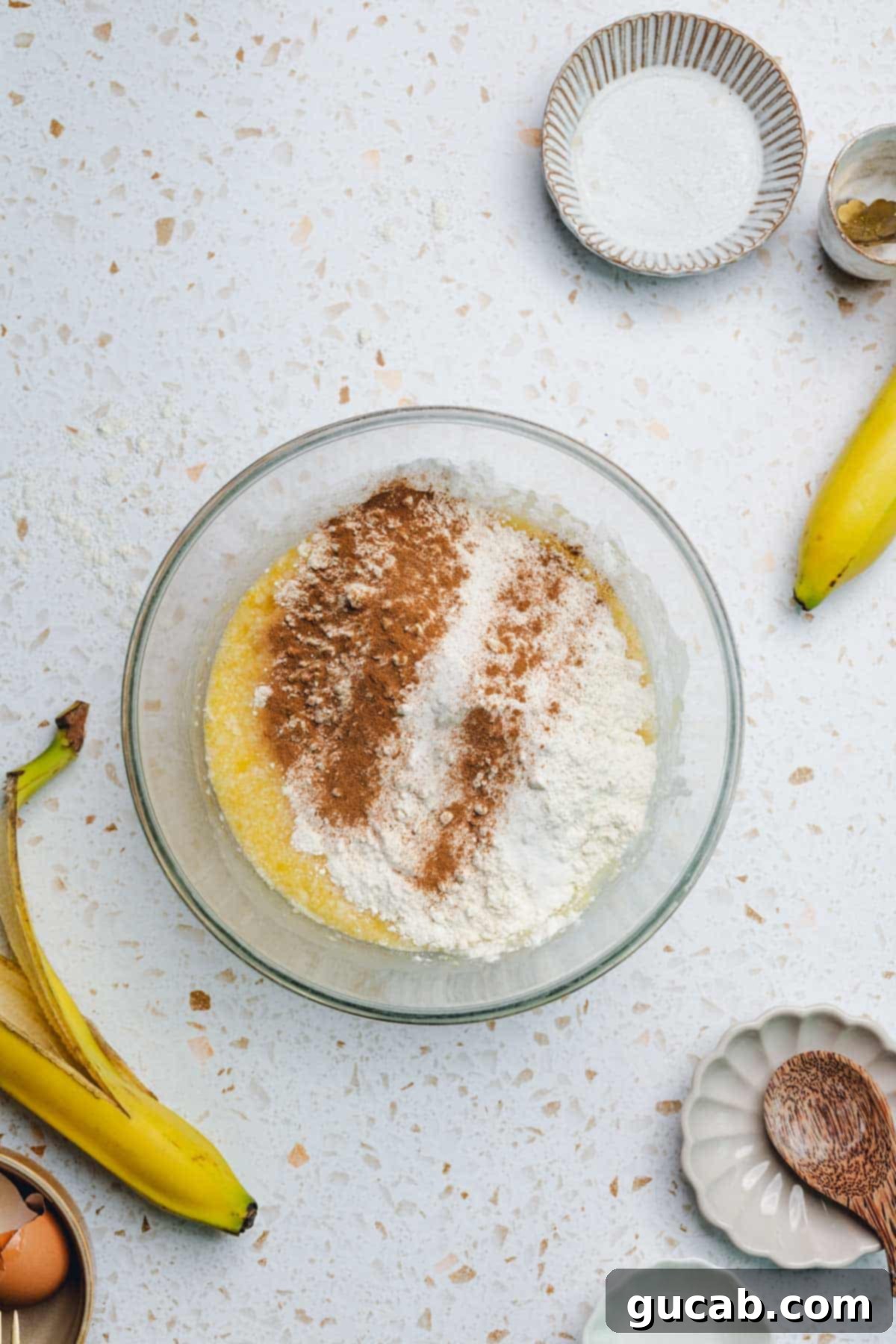 The combined wet ingredients in a bowl with flour and cinnamon sprinkled on top, ready for final mixing.