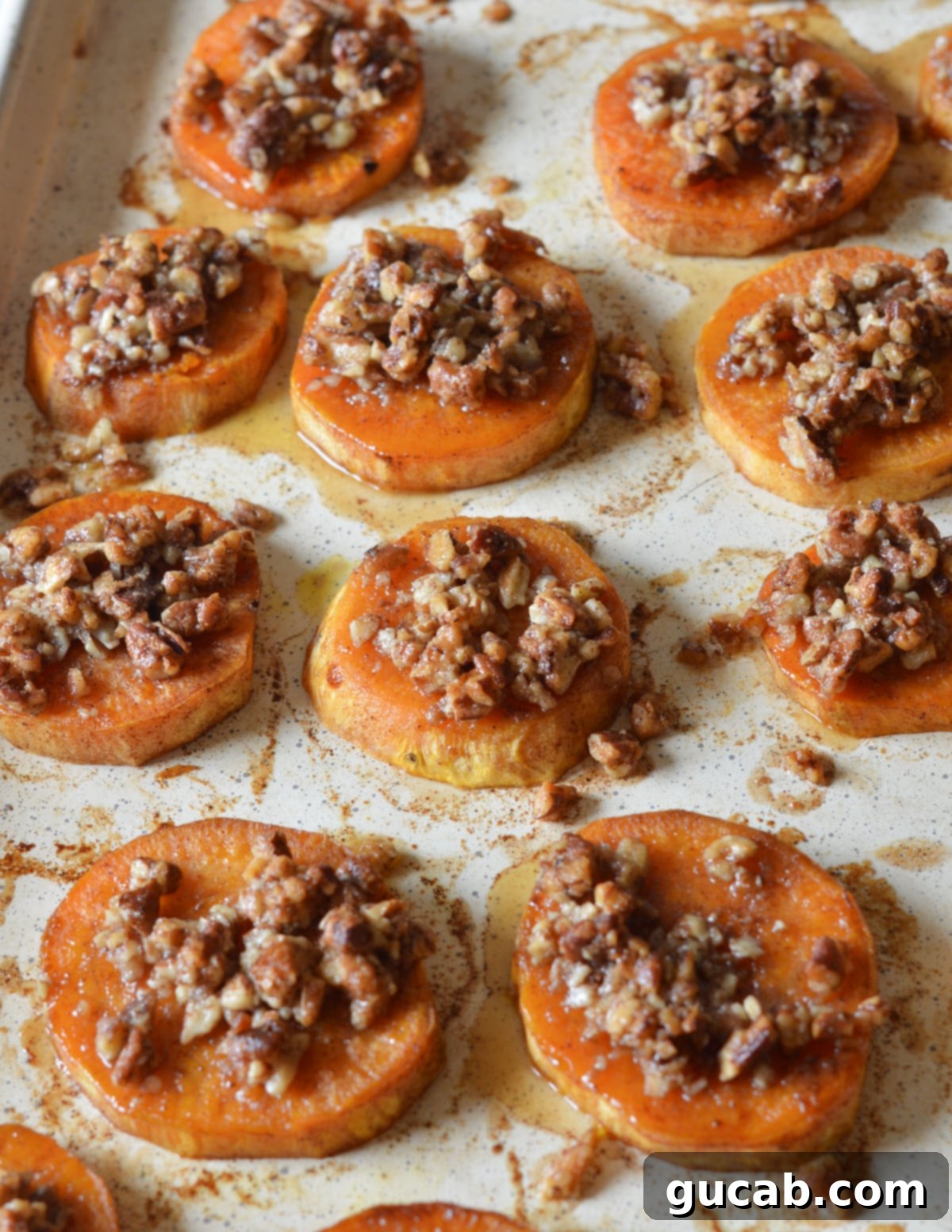 Platter of perfectly roasted sweet potato slices, each topped with a generous sprinkle of golden candied pecans.