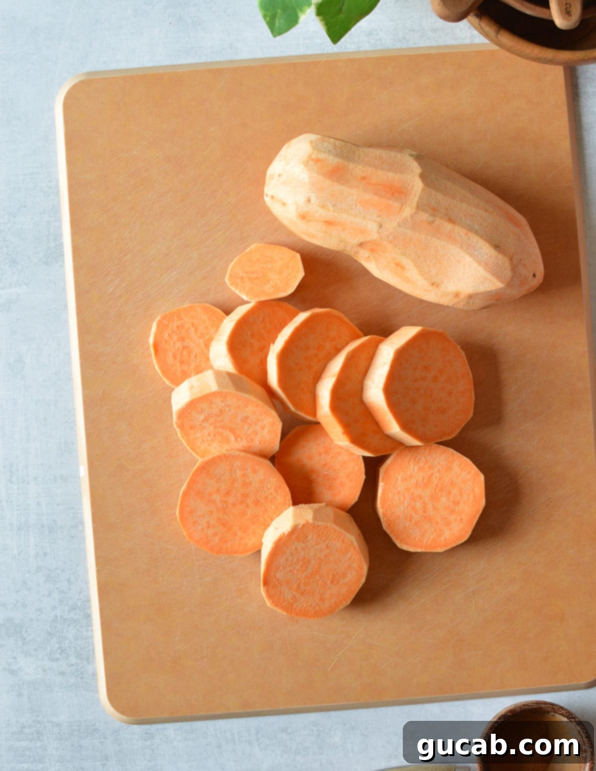 Neatly sliced raw sweet potatoes arranged on a wooden cutting board, ready for seasoning.