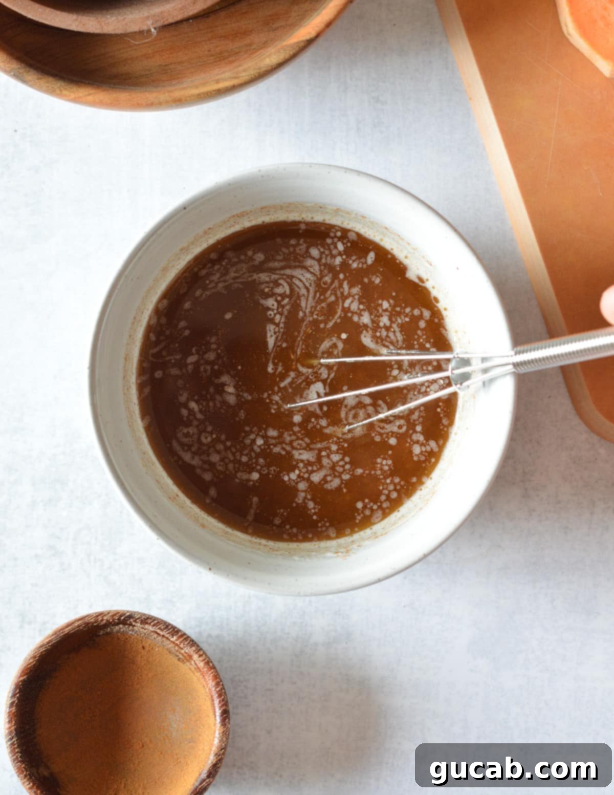 A mini whisk actively stirring the melted butter, maple syrup, and cinnamon mixture in a small bowl.