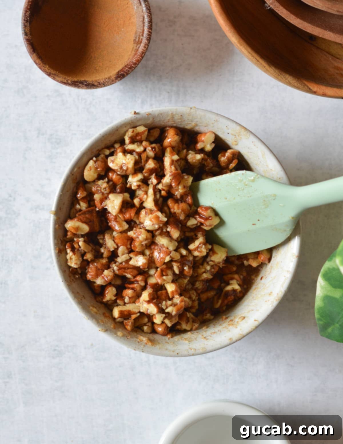 A bowl filled with finely chopped pecans, glistening with a coating of maple syrup and butter mixture.