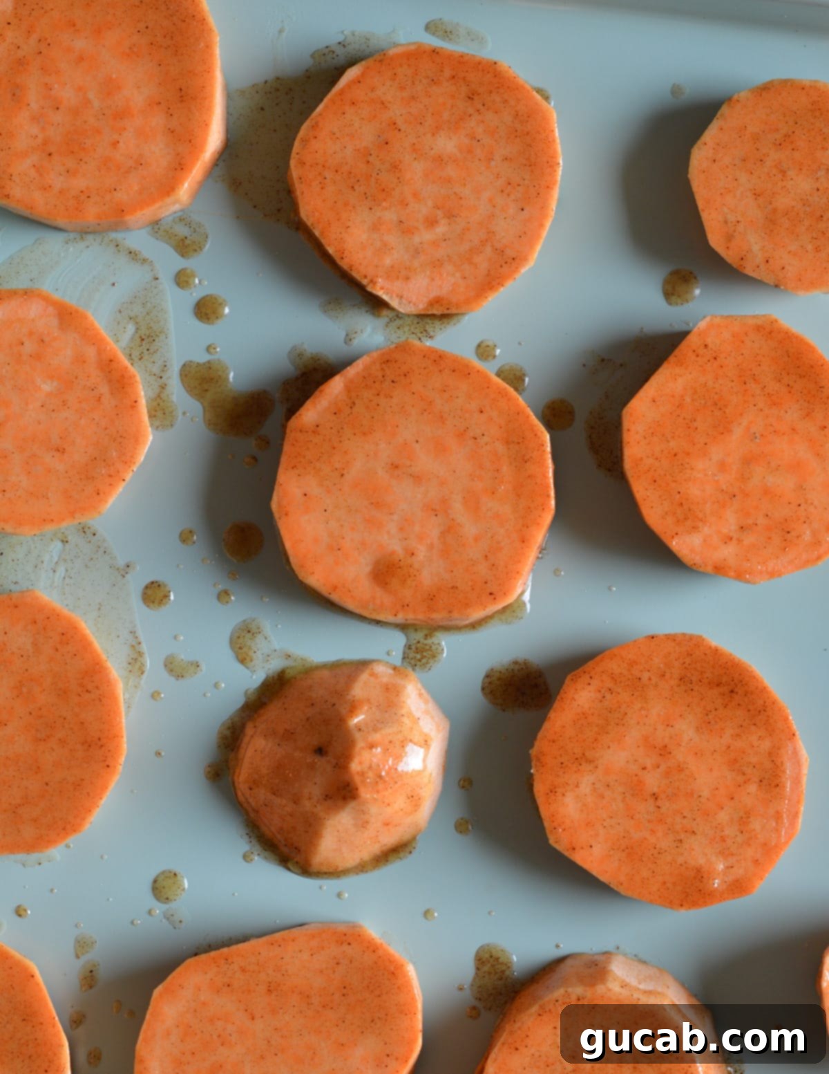 Close-up of raw sweet potato slices on a baking sheet, brushed generously with maple syrup and butter.