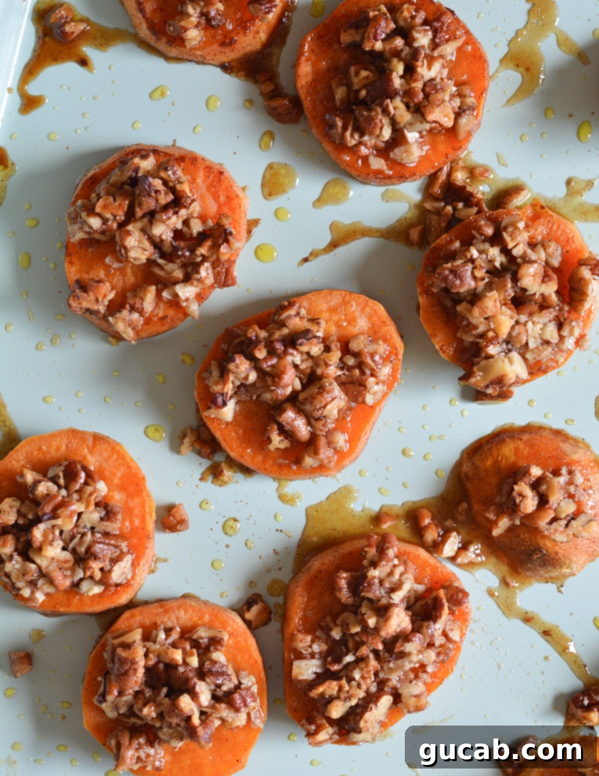 Baking sheet with half-roasted sweet potato slices, now topped with candied pecans, ready for the final bake.