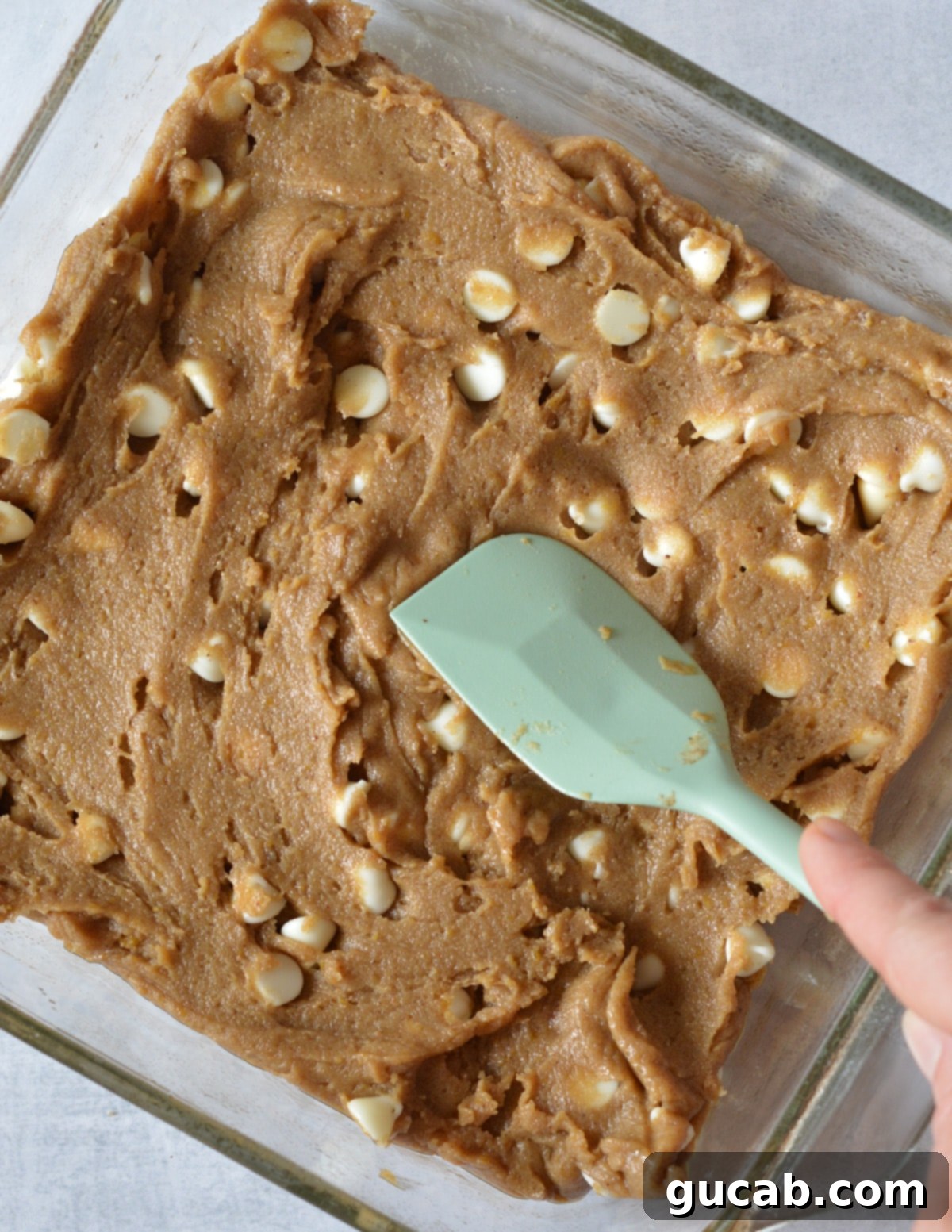 spatula spreading gluten free brownie dough into a glass baking dish.