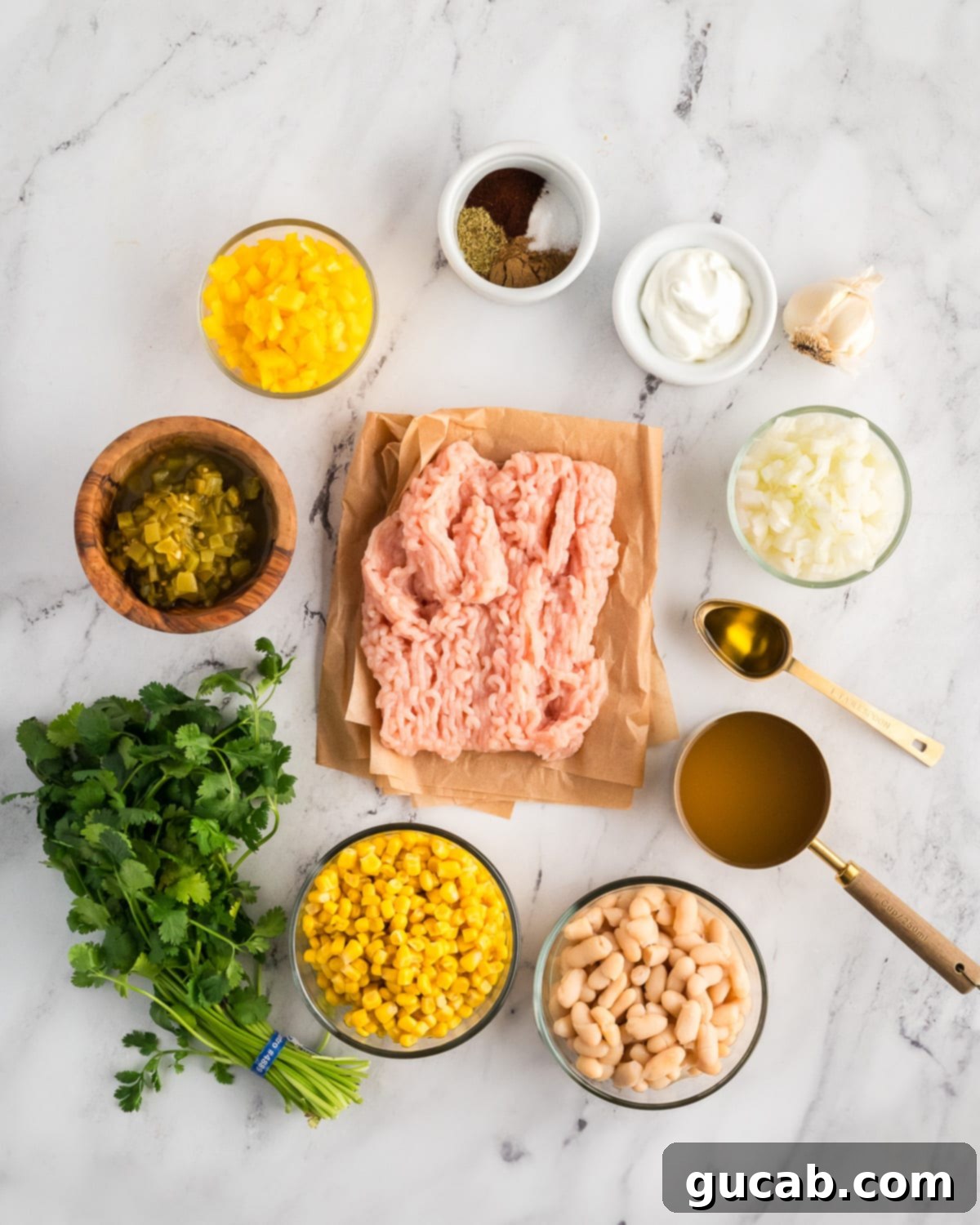 Creamy White Ground Chicken Chili 3 A vibrant display of fresh ingredients for white ground chicken chili including ground chicken, various spices, diced bell pepper, diced onion, sour cream, garlic, green chiles, chicken stock, olive oil, cilantro, corn, and white beans.