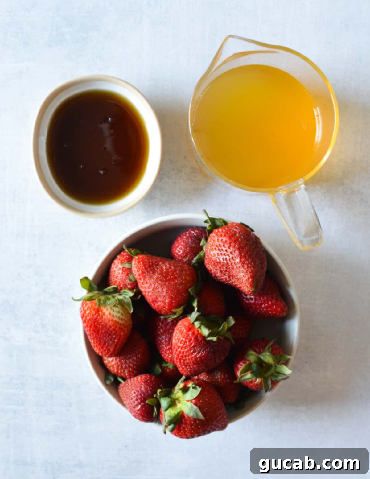 A vibrant display of fresh strawberries, a bottle of clear passion fruit juice, and golden maple syrup, the three simple ingredients for homemade popsicles.