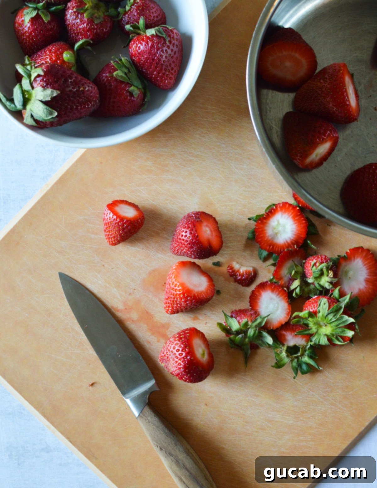 Fresh strawberries with their green tops removed and hulled, ready for the popsicle mixture, neatly arranged on a wooden cutting board.