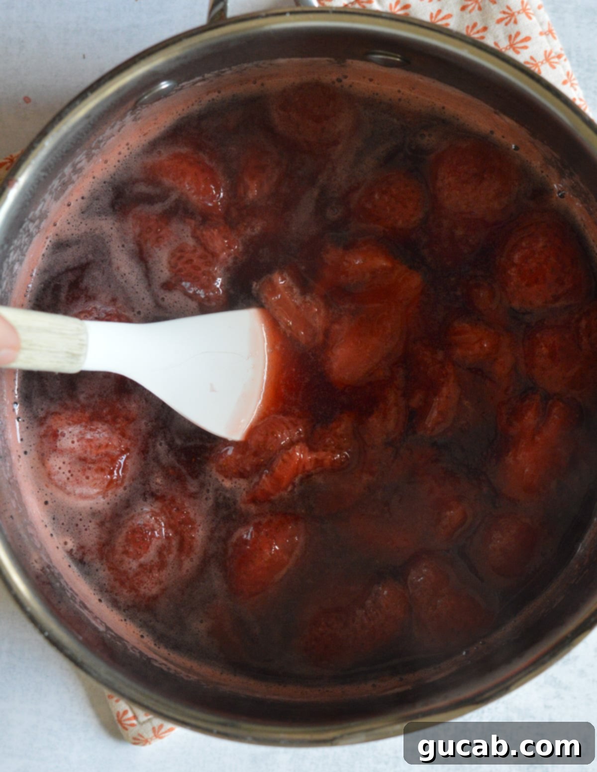 Cooked strawberry mixture in a saucepan, after simmering, with a spatula resting inside, showing its rich, reduced consistency before blending.