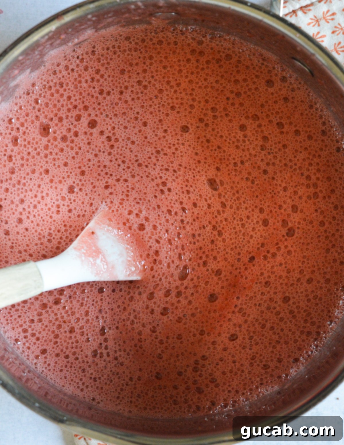 Smooth, vibrant red strawberry mixture in a saucepan after being blended, ready to be transferred to popsicle molds.