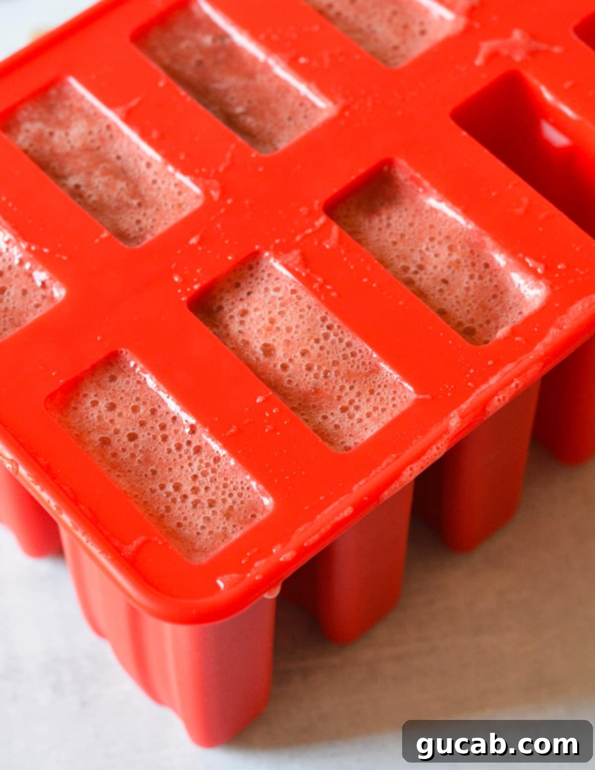 A popsicle mold filled to the brim with the rich, red strawberry mixture, patiently awaiting popsicle sticks and the freezer.