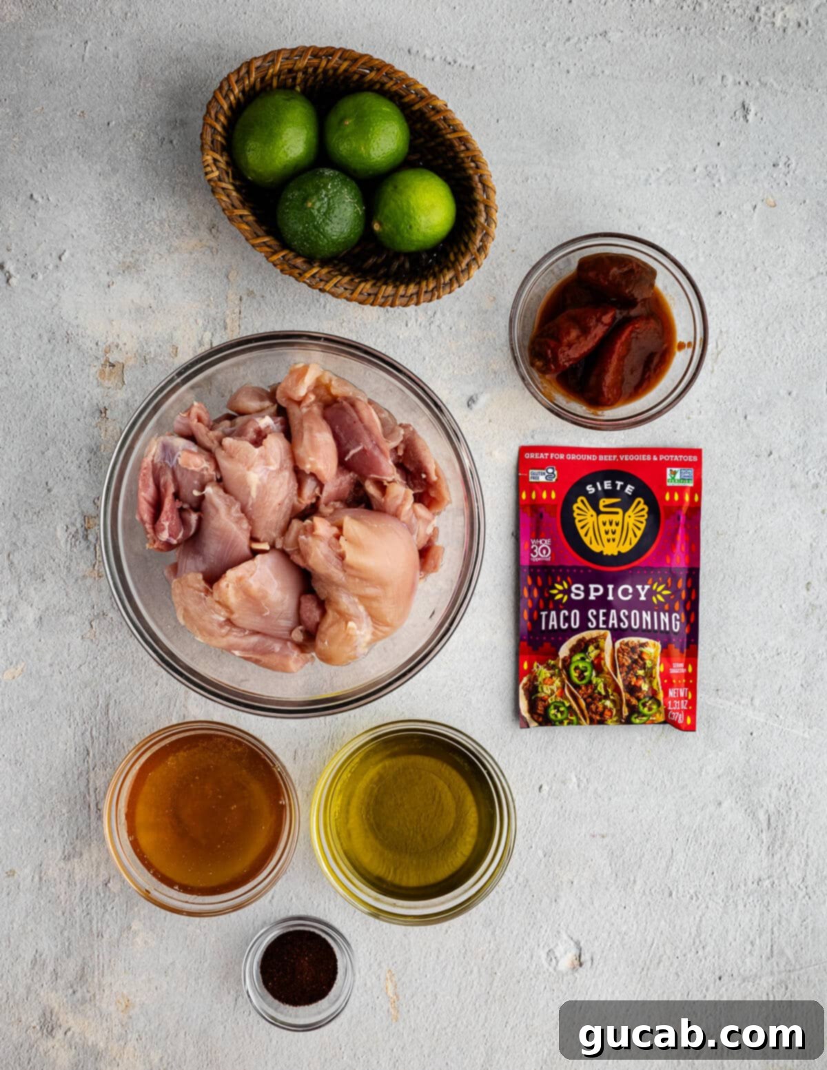 A selection of key ingredients laid out for honey chipotle chicken thighs recipe, including chicken thighs, a jar of chipotles in adobo, a bottle of olive oil, honey, and spice jars.