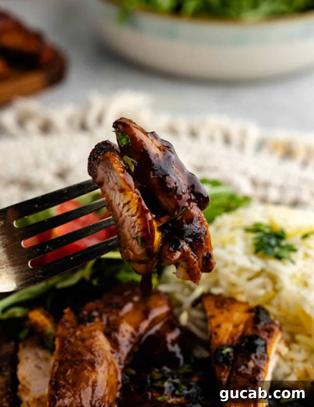 A close-up of a fork holding a piece of caramelized honey chipotle chicken, showing its juicy interior.