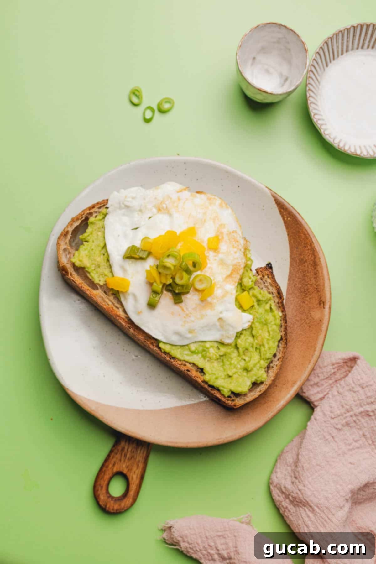 A close-up of the assembled avocado toast, with mashed avocado on toast, topped with a fried egg, ready for sauce and pickled vegetables.