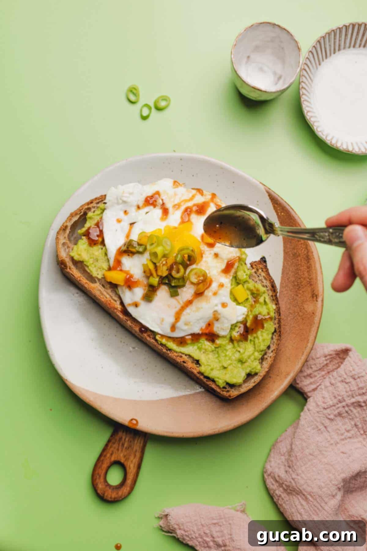 Close-up of the finished avocado toast, showcasing the runny egg yolk, chipotle sauce, and pickled vegetables.