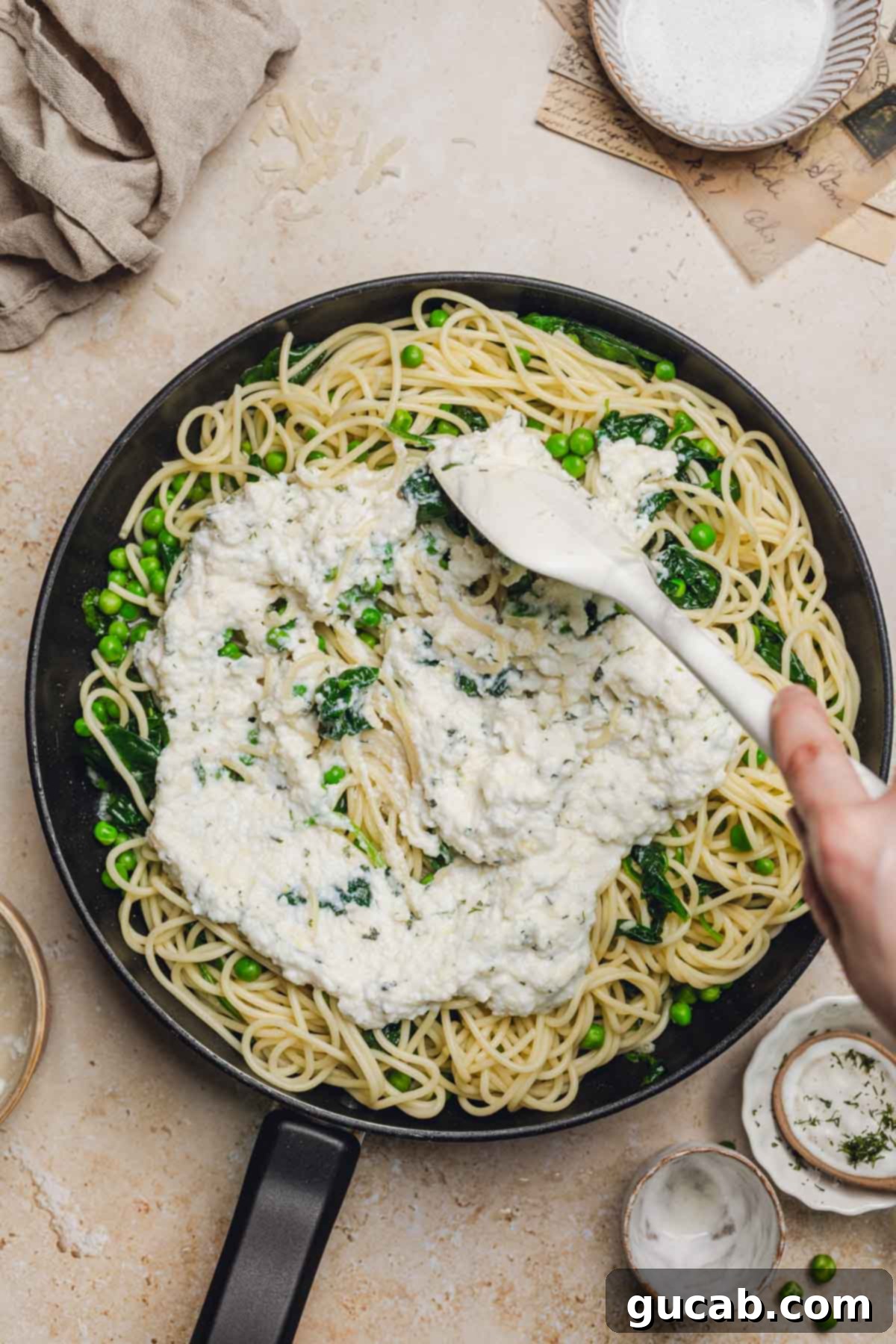 A spatula stirring the rich ricotta and Parmesan sauce into the skillet with noodles and spinach, creating the final creamy texture.