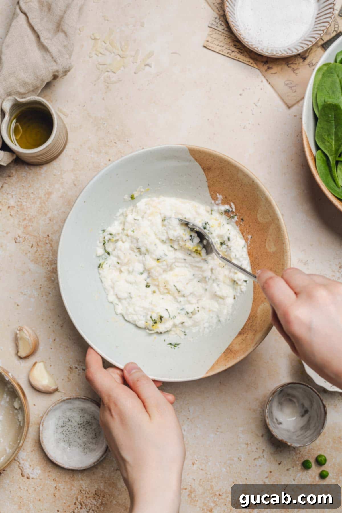 A hand mixing the ricotta, Parmesan, fresh herbs, and lemon juice in a bowl with a spoon, creating the sauce base.