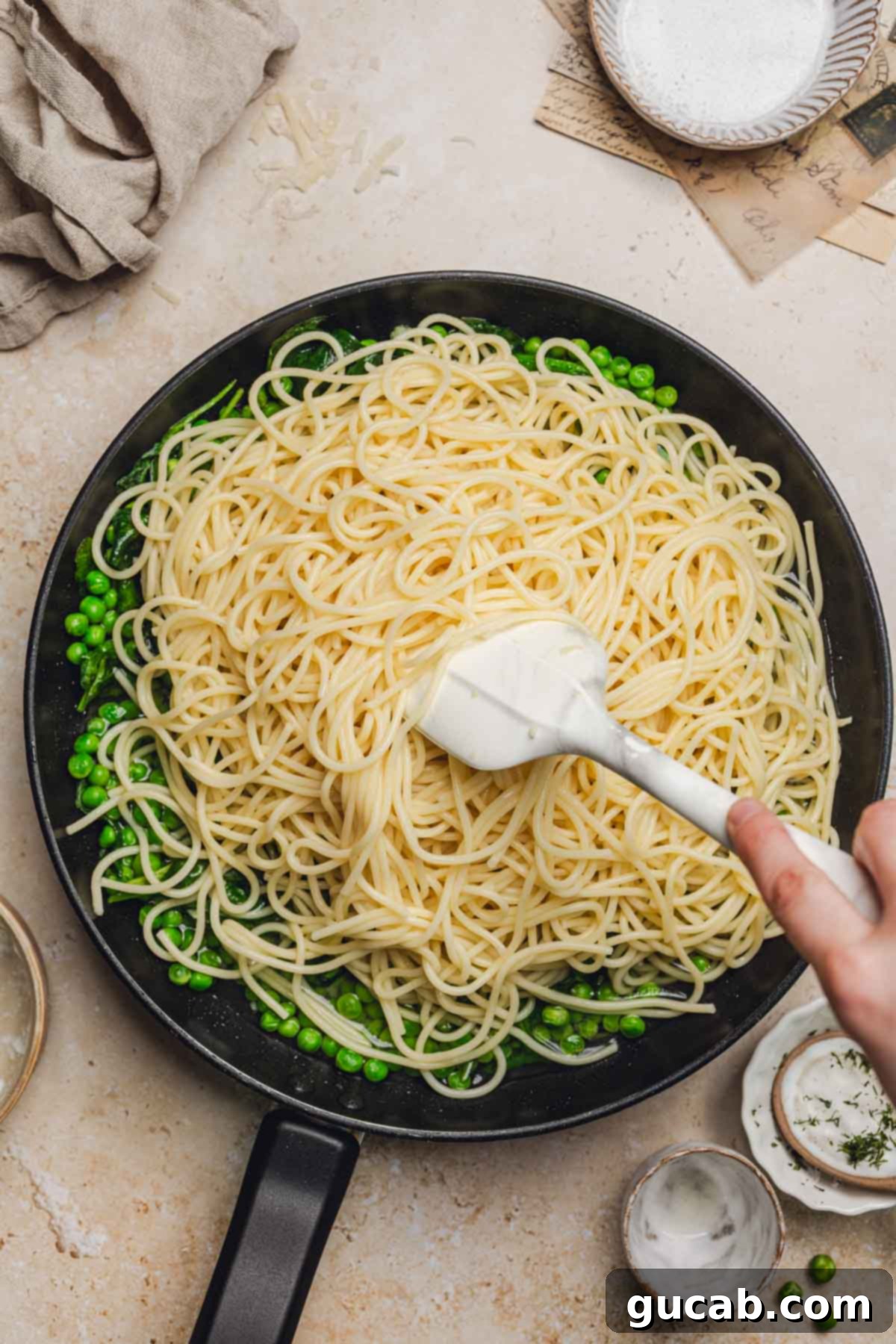 A spatula stirring the pasta with the spinach and peas in the skillet, ensuring everything is well combined.