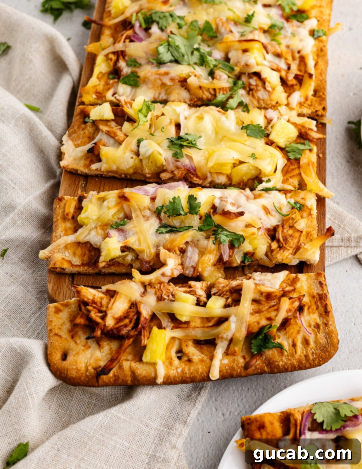 Close-up of a fully assembled BBQ Chicken Flatbread with pineapple, chicken, cheese, and red onion, before baking. It shows a vibrant mix of toppings on a light flatbread base.