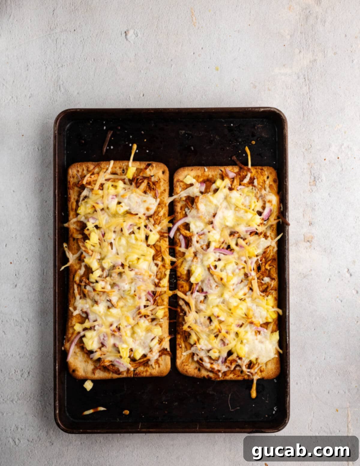 Freshly baked Hawaiian BBQ Chicken Flatbreads on a sheet pan, hot out of the oven, with melted, bubbly cheese and golden-brown crusts.