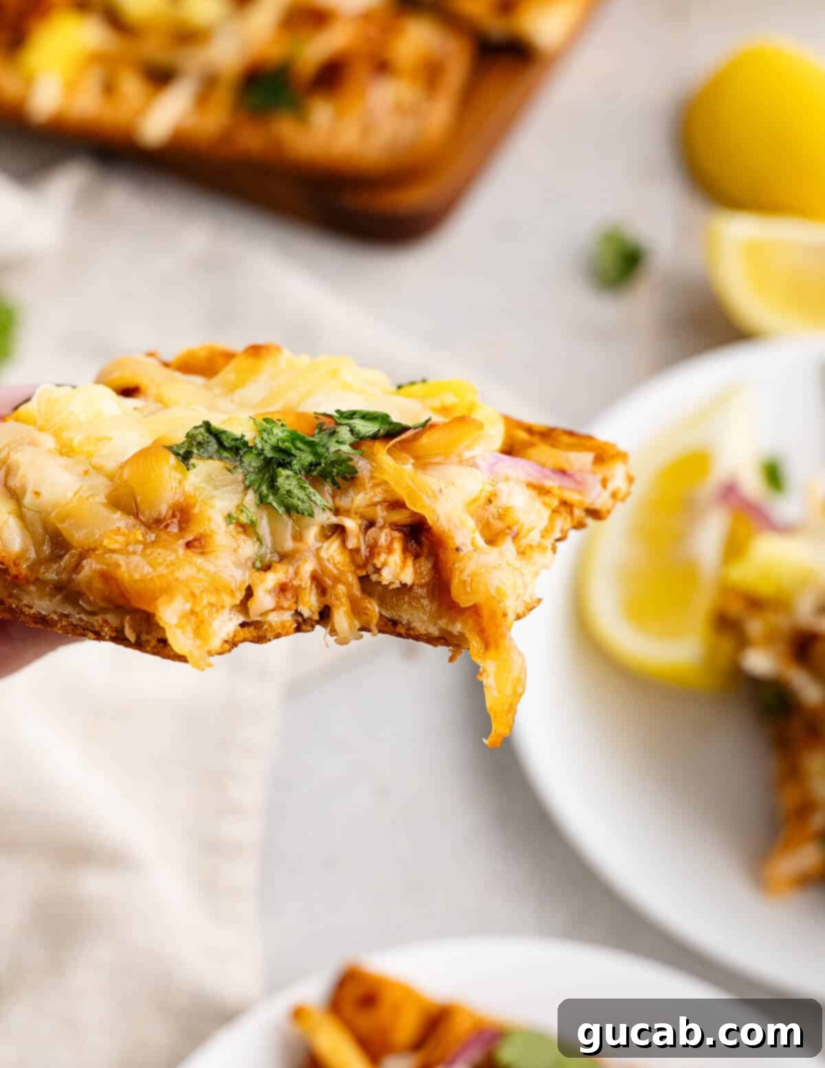 A hand holding a perfectly baked slice of BBQ chicken flatbread, showcasing the melted cheese, crispy crust, and colorful toppings ready to be enjoyed.