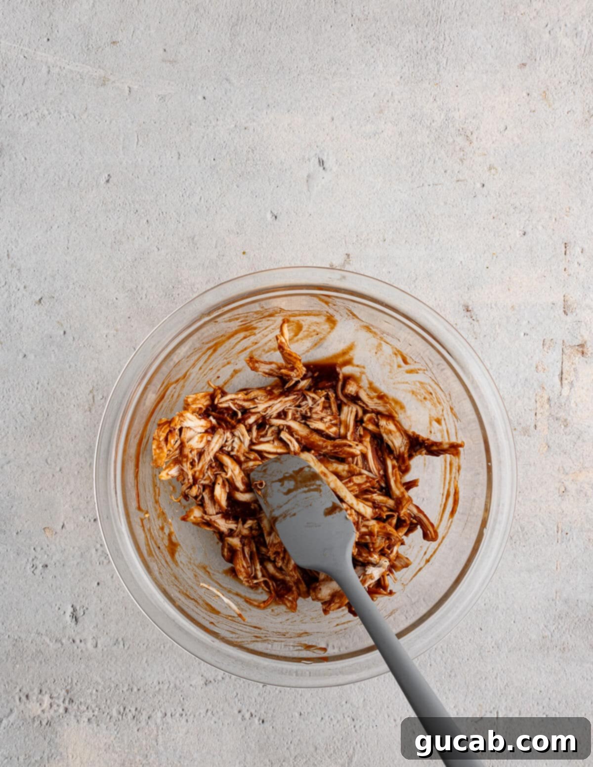 A bowl of tender shredded chicken mixed thoroughly with a rich barbecue sauce, ready for the flatbreads.