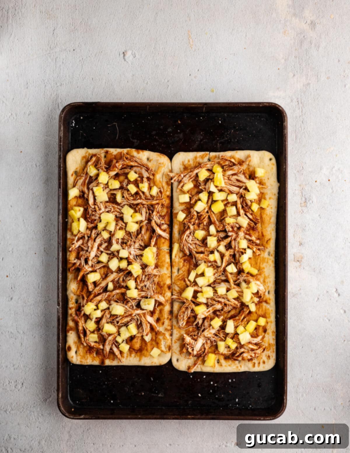 Applying a base layer of barbecue sauce to a par-baked flatbread, ensuring full coverage.