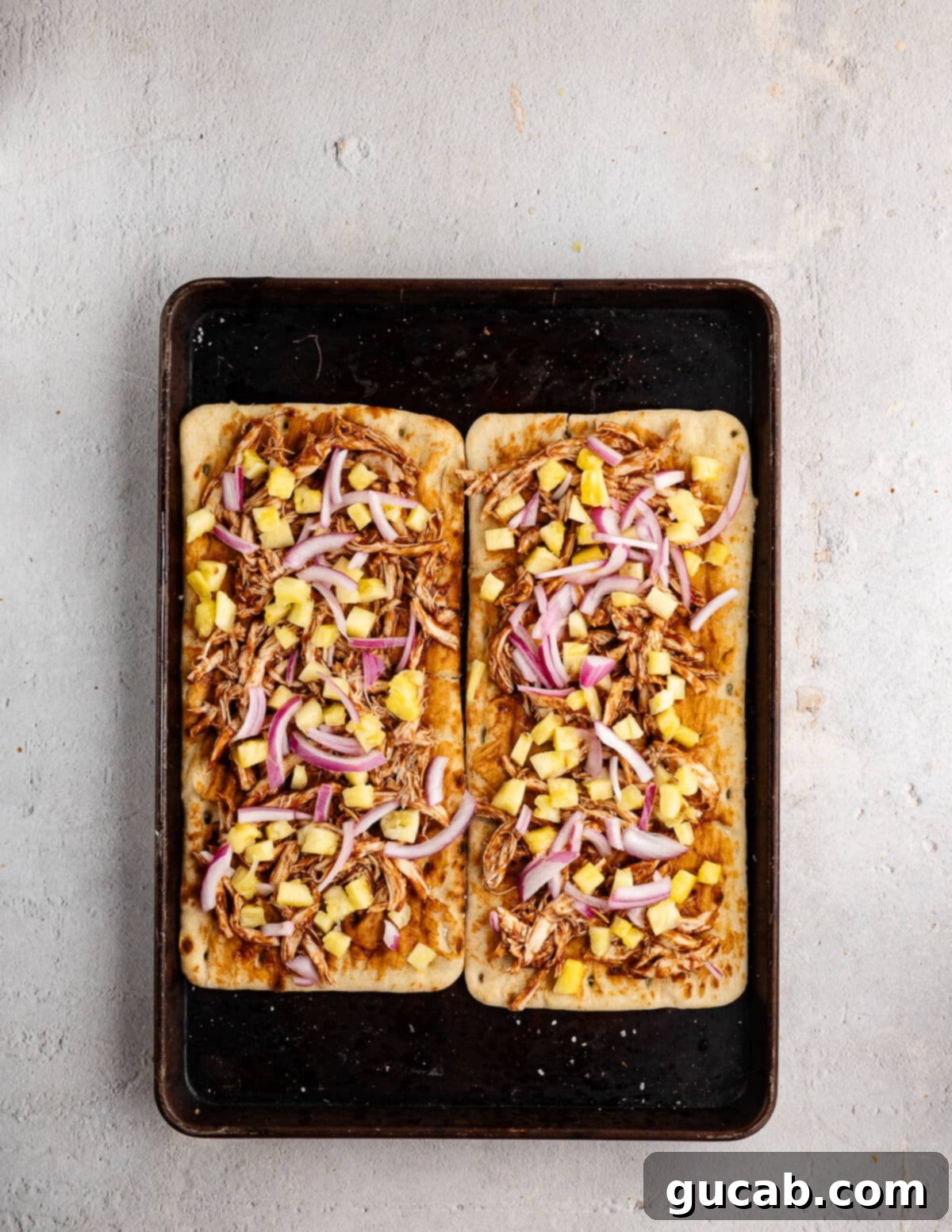 Layering barbecue chicken and pineapple onto a flatbread base, ensuring a balanced distribution of ingredients.