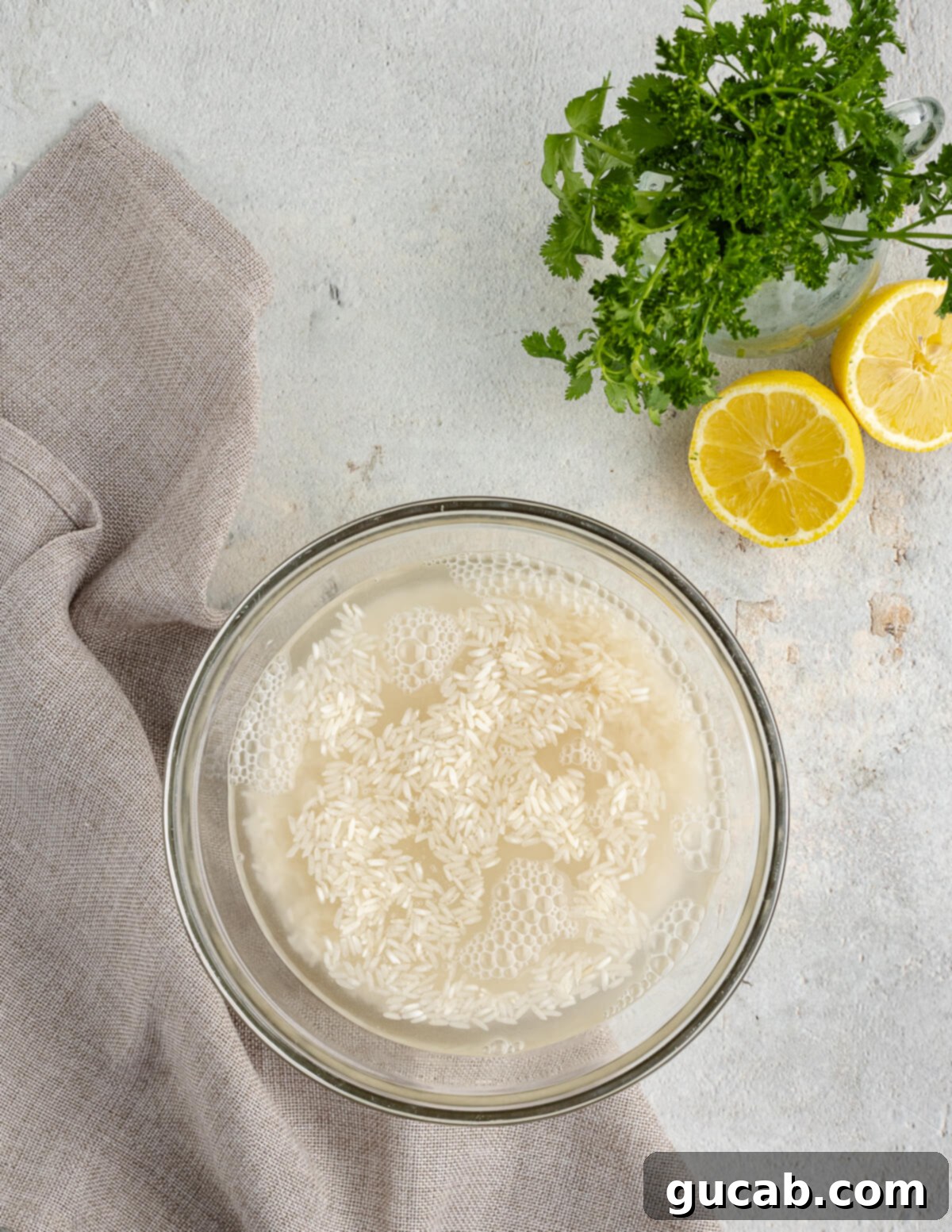 White rice soaking in cool water in a clear glass bowl, preparing for cooking.