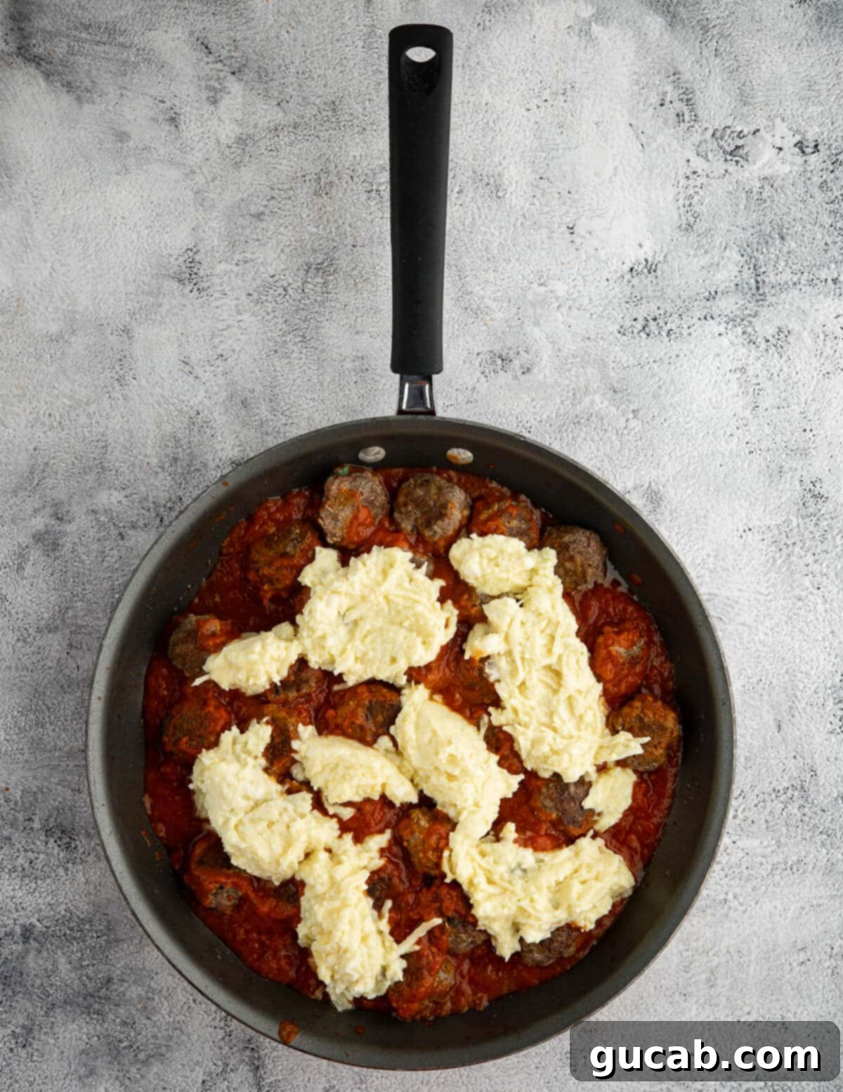 One-Pan Cheesy Meatballs 11 Saucy meatballs in a pan, topped with generous dollops of the creamy ricotta cheese mixture, ready for baking.