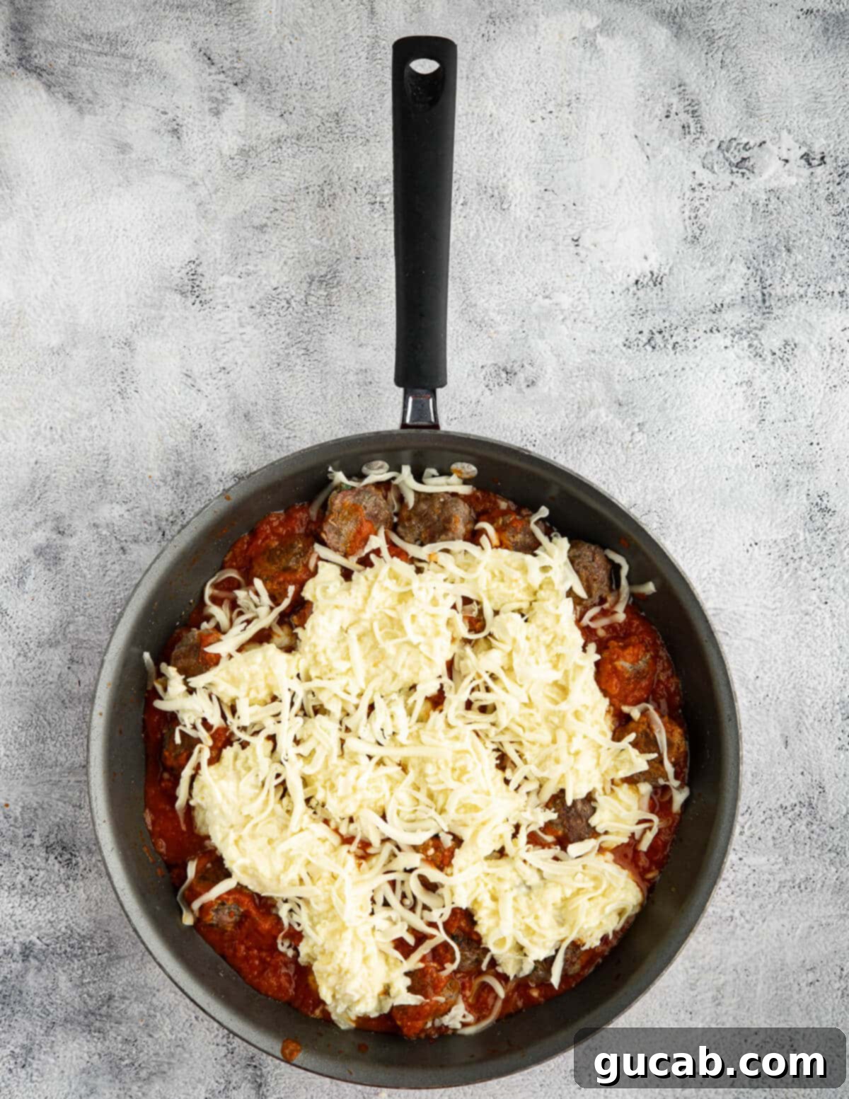 One-Pan Cheesy Meatballs 12 Saucy meatballs in a pan, layered with ricotta and then covered with a generous blanket of shredded mozzarella cheese, ready for the oven.