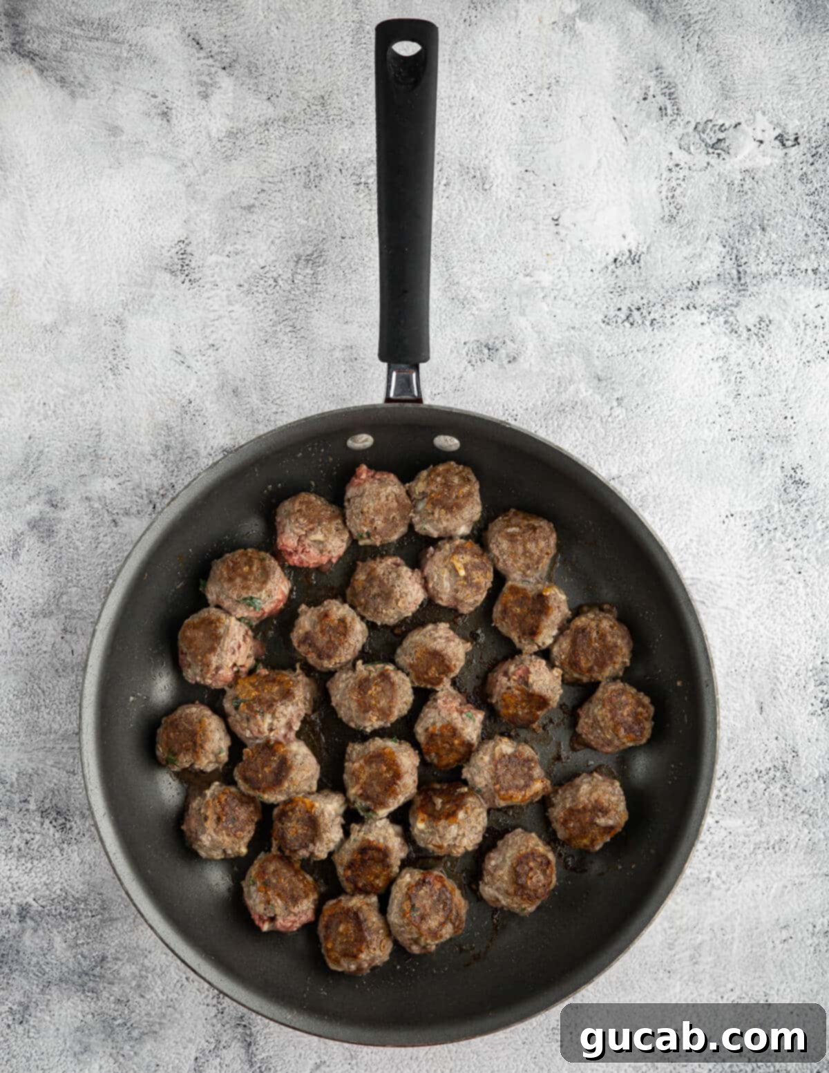 One-Pan Cheesy Meatballs 9 Golden-brown meatballs, partially cooked, resting in a skillet after being browned on the stovetop.