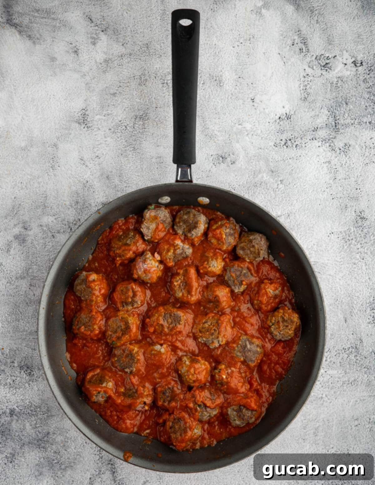 One-Pan Cheesy Meatballs 10 Browned meatballs coated generously in rich marinara sauce within a skillet, preparing for the next step.