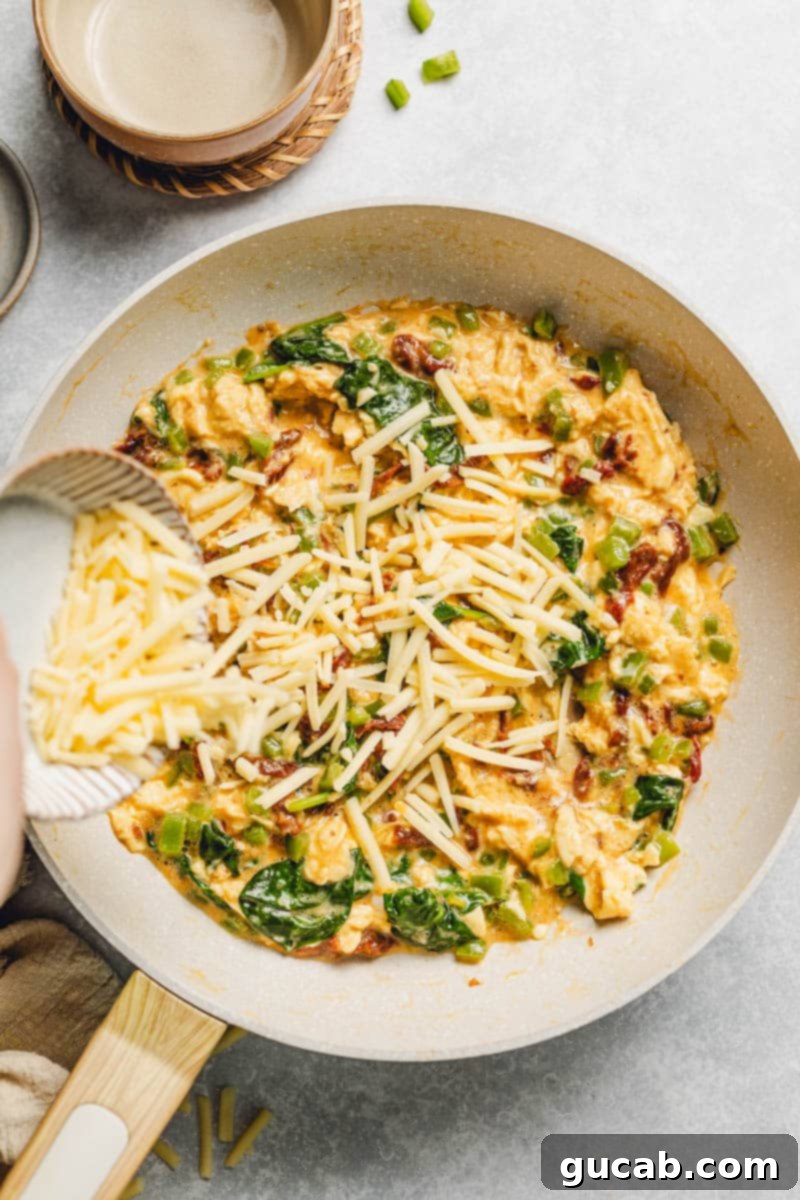 pouring shredded cheese into a veggie egg scramble.