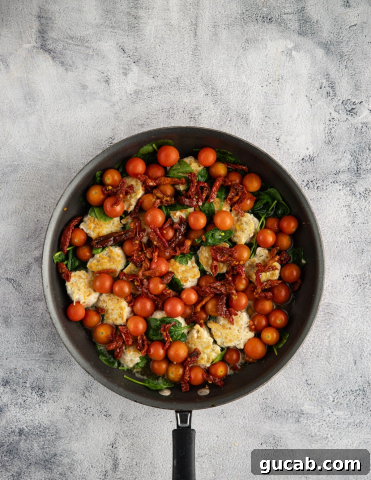 chicken meatballs, tomatoes, sun-dried tomatoes, spinach, and garlic in a skillet. 
