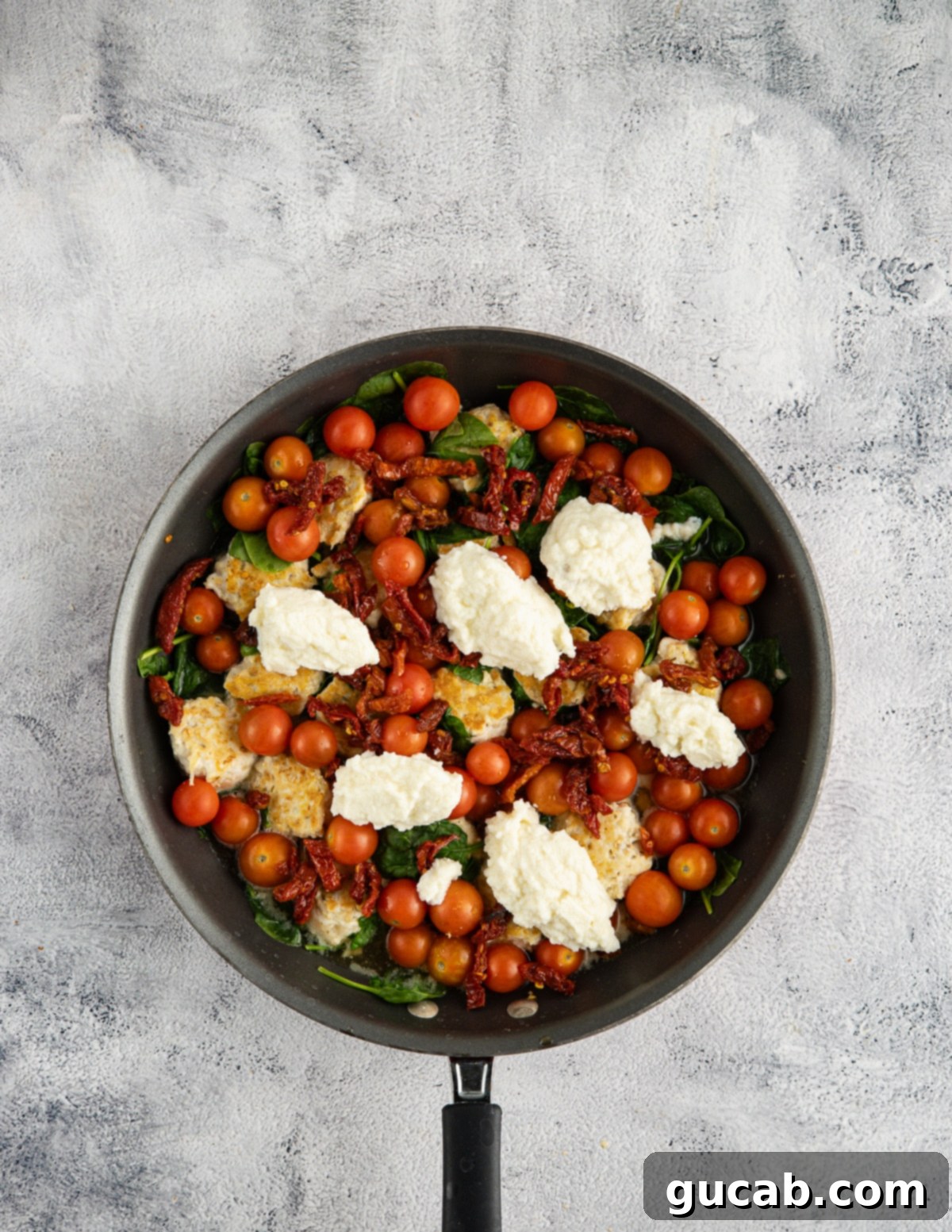 chicken meatballs, sun-dried tomatoes, tomatoes, spinach, and garlic in a skillet with dollops of ricotta on top. 