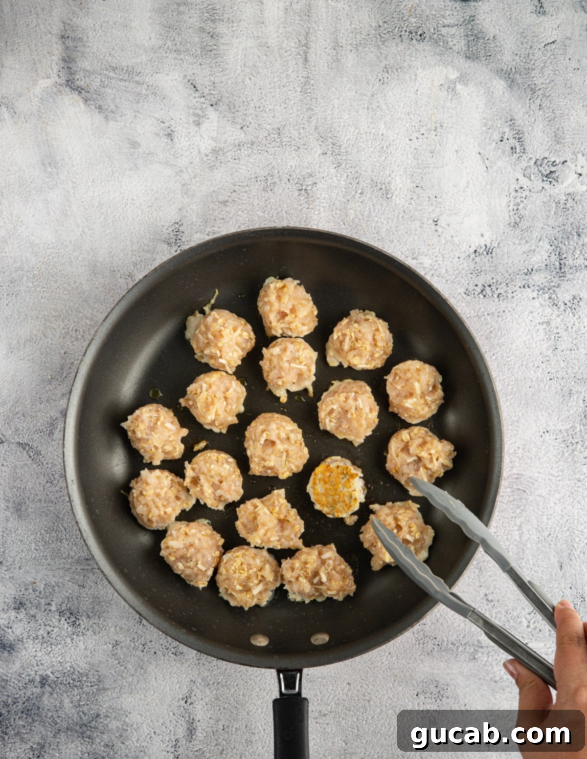 The Ultimate Date Night Chicken Meatballs 7 Raw, unbrowned chicken meatballs arranged in a skillet.