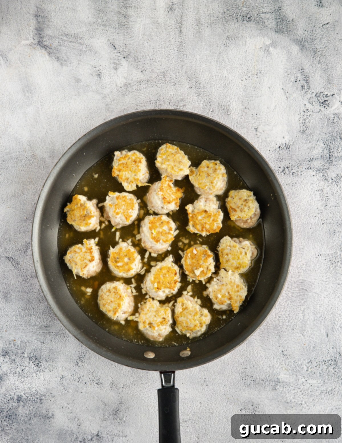 The Ultimate Date Night Chicken Meatballs 8 Browned chicken meatballs in a skillet, partially cooked.