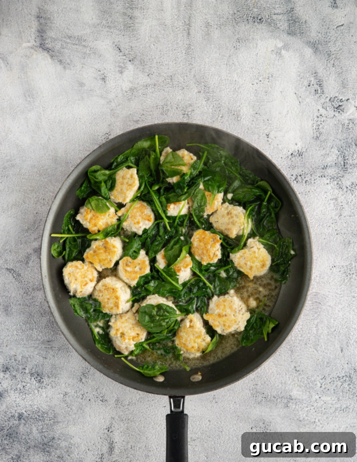 The Ultimate Date Night Chicken Meatballs 9 A skillet with chicken meatballs, chicken stock, and wilted spinach in it, before adding tomatoes.