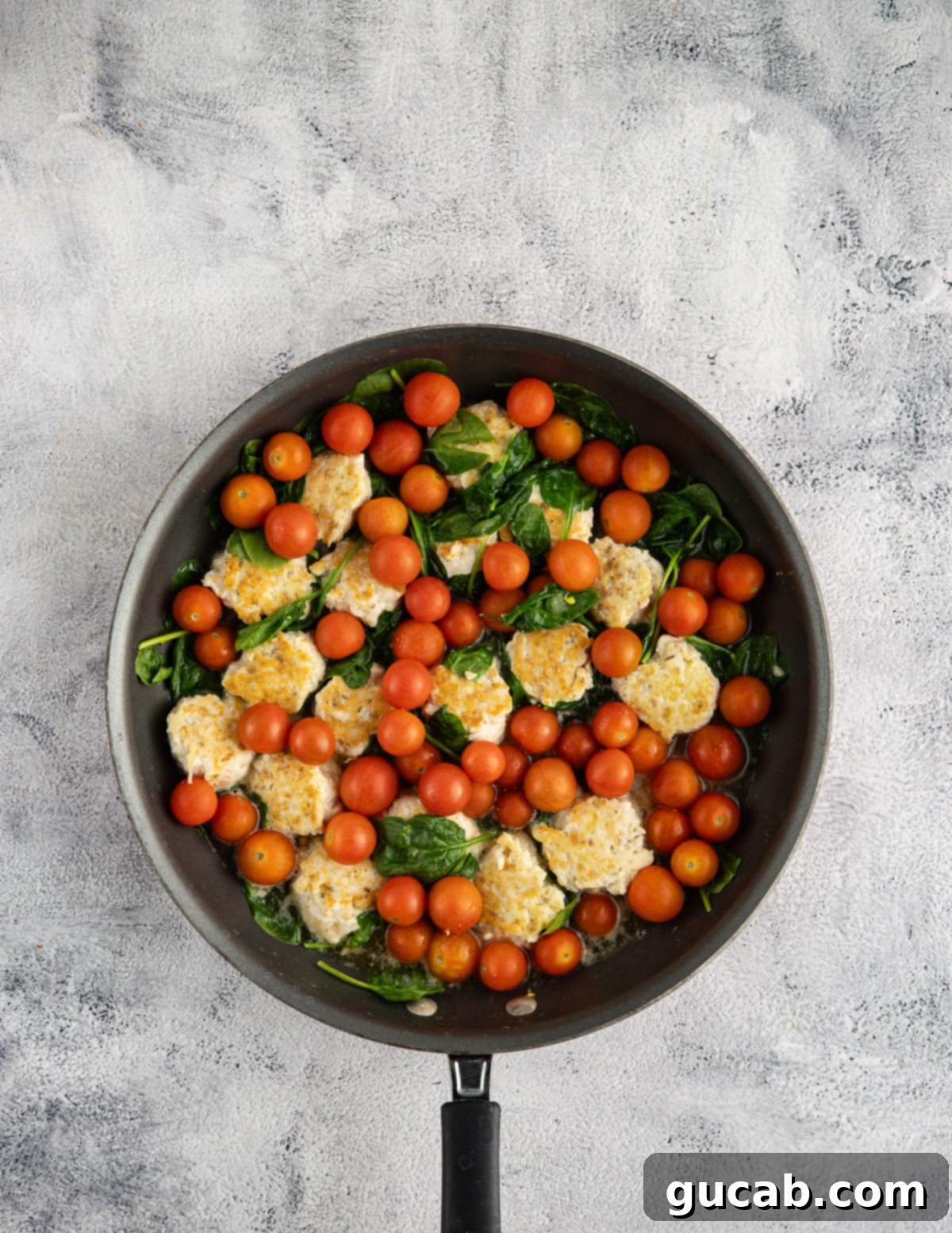 a skillet with chicken meatballs, tomatoes, sun-dried tomatoes, and spinach in it. 