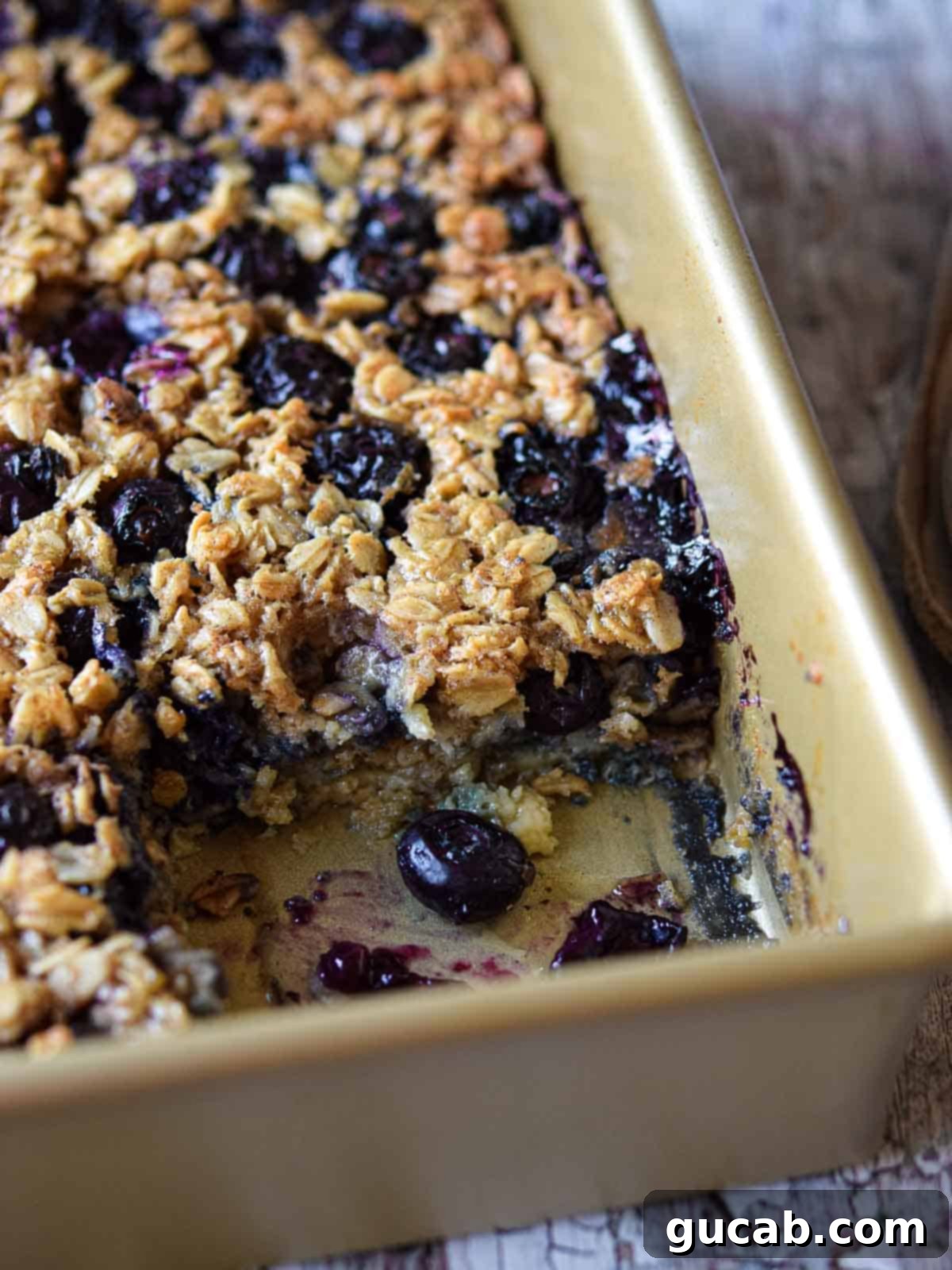A rustic baking dish filled with golden-brown blueberry baked oatmeal, showcasing juicy blueberries nestled within a comforting oat base.