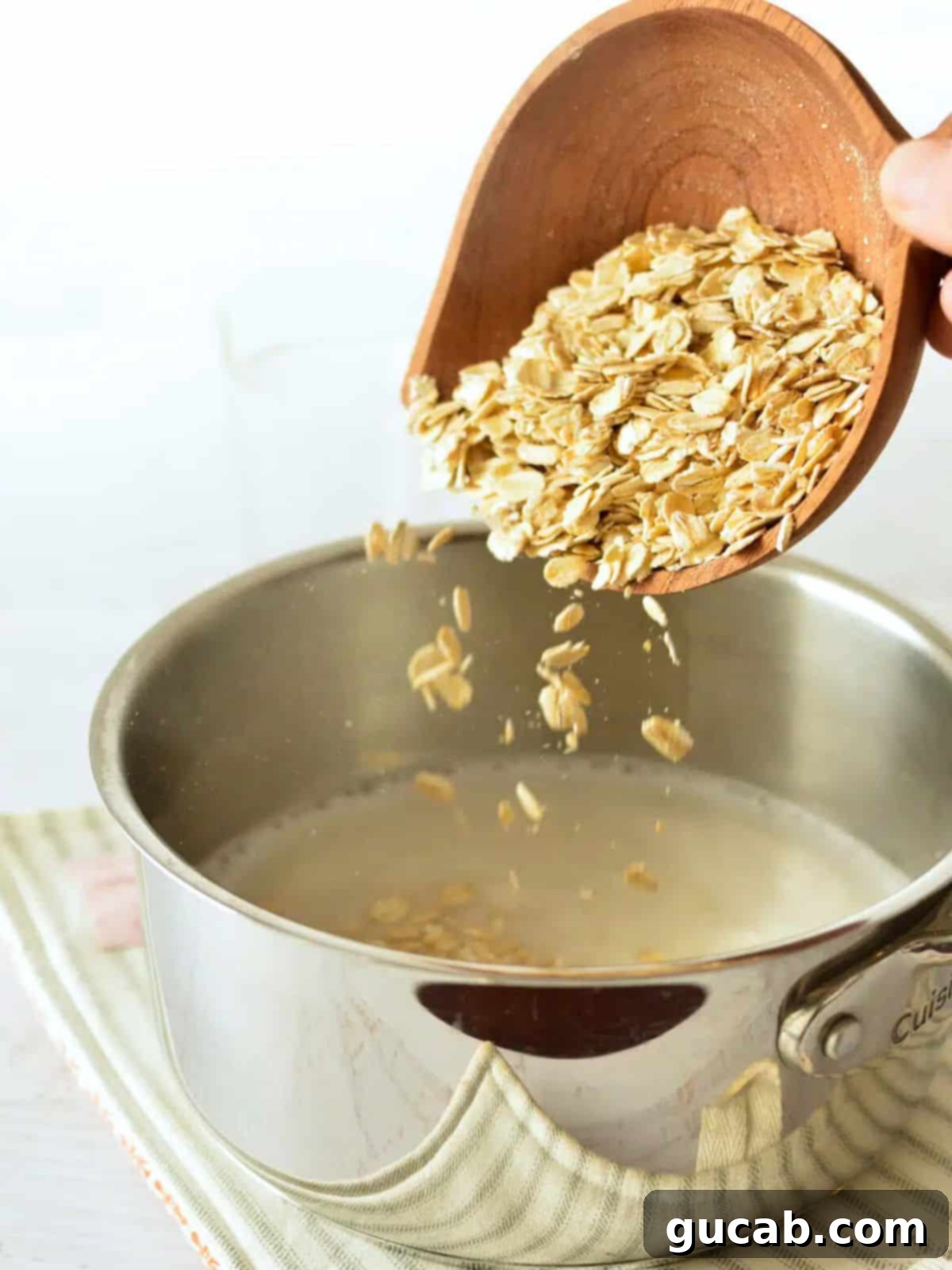 A hand pouring old-fashioned oats into a pot, where water and milk are already simmering, ready for cooking.
