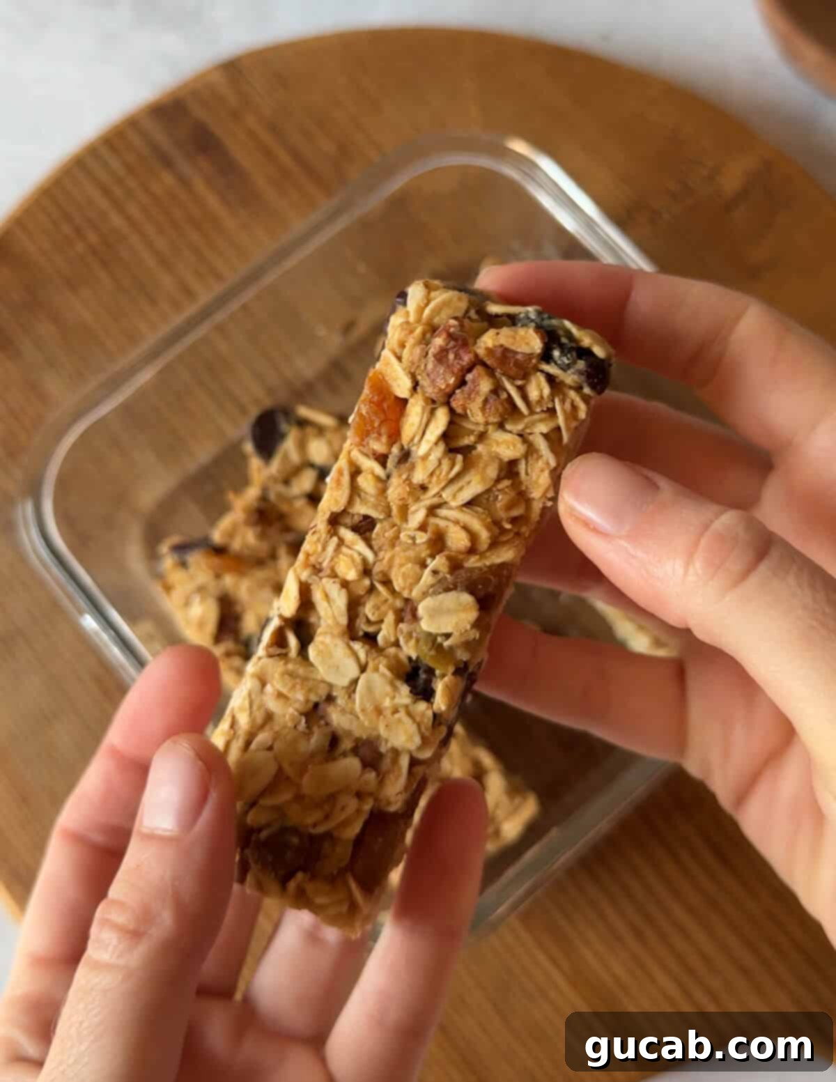 A hand thoughtfully holding a freshly made homemade granola bar, showcasing its dense texture and visible wholesome ingredients like oats, nuts, and chocolate chips.