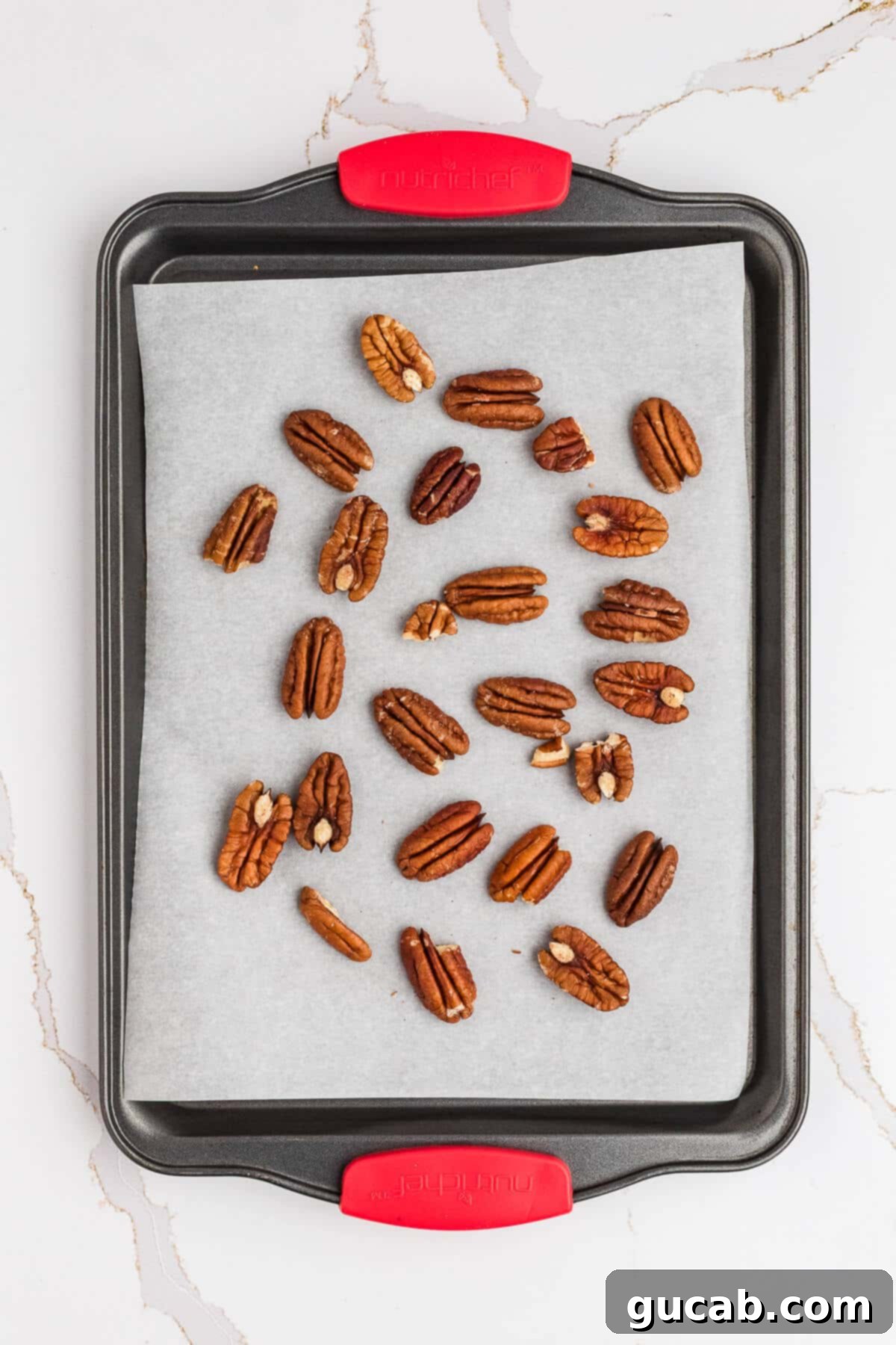 Pecan halves spread out on a sheet pan lined with parchment paper, ready for toasting to enhance their nutty flavor.