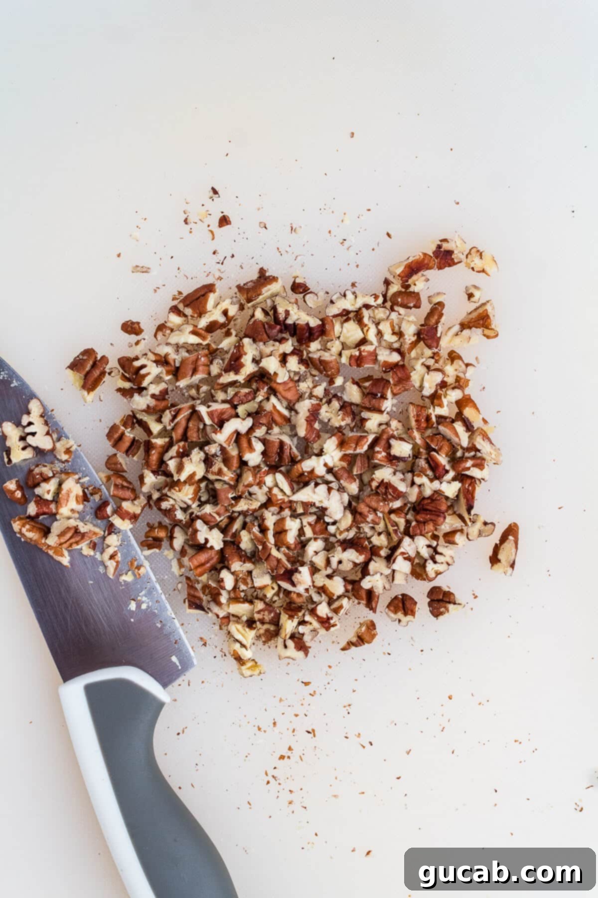 Freshly chopped toasted pecans on a wooden cutting board, finely broken down and ready to be incorporated into the granola bar mixture for even distribution.