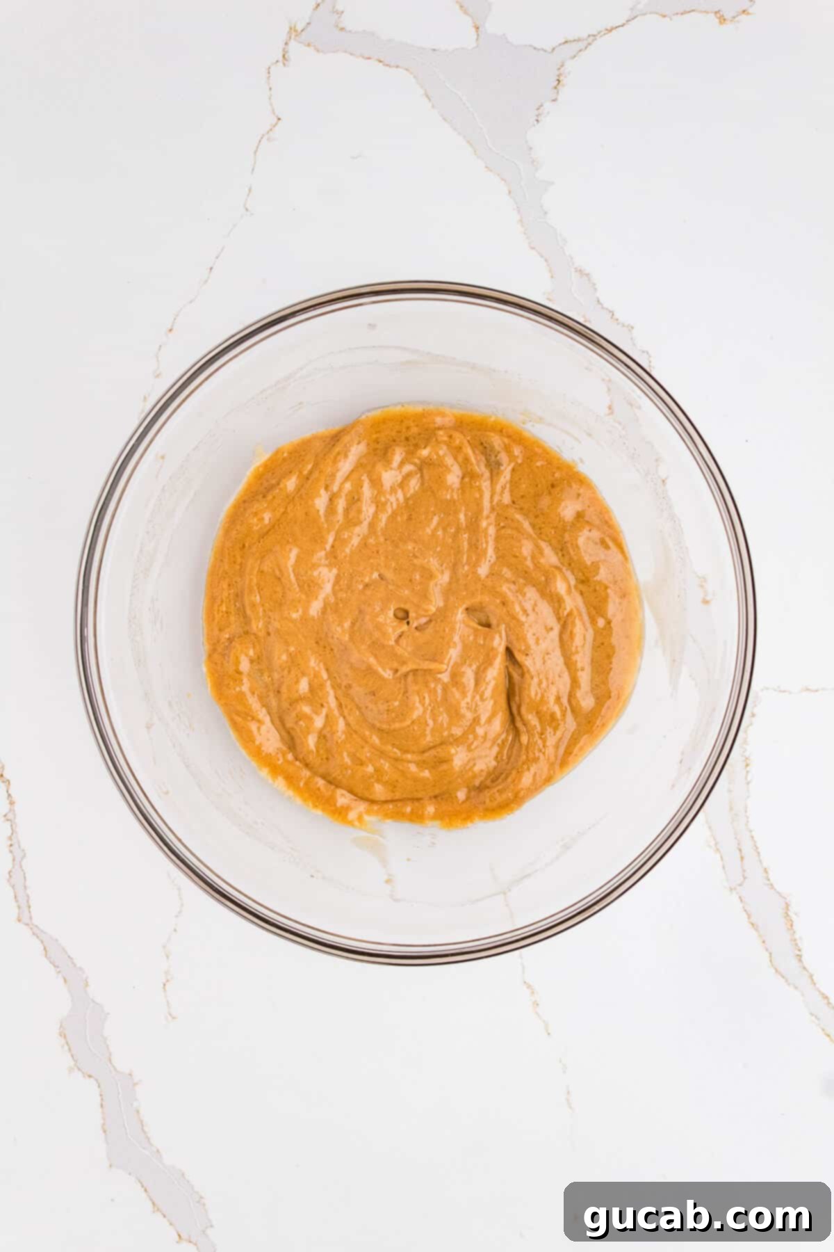 A bowl containing a smooth, creamy mixture of honey and peanut butter, perfectly blended and ready to be combined with dry ingredients.