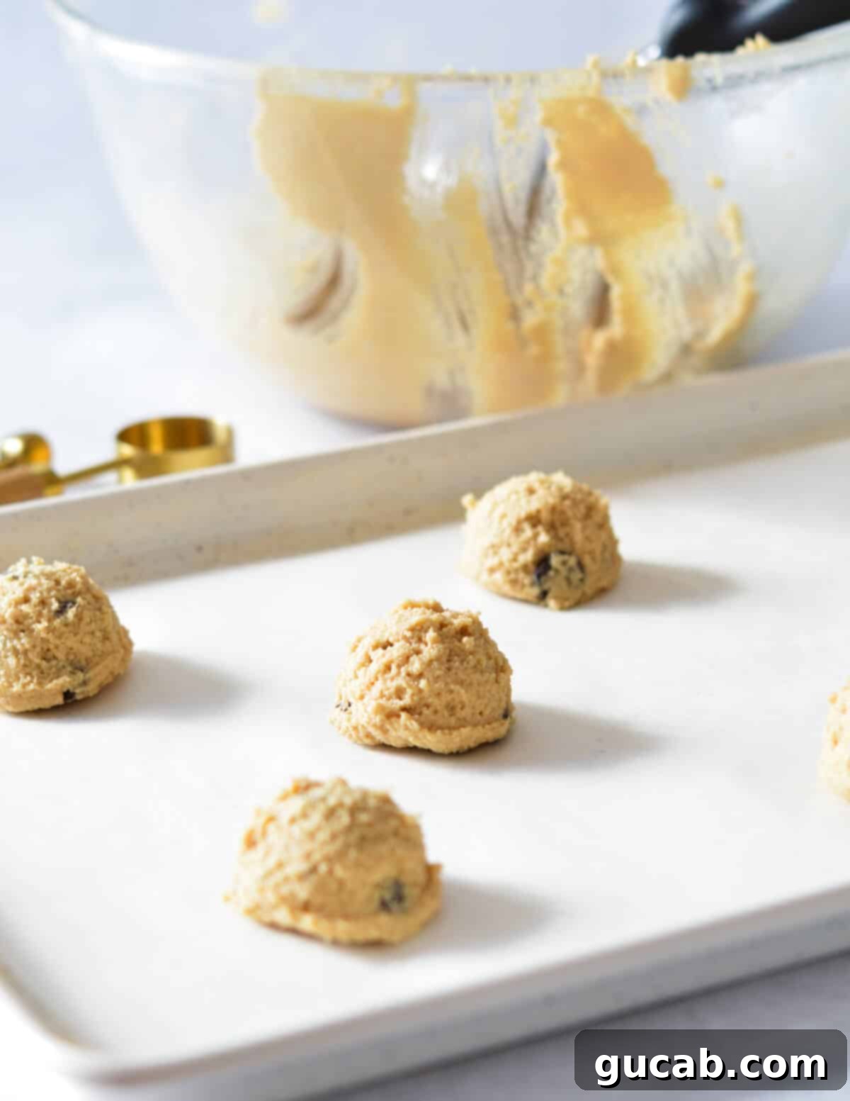 Uniform balls of peanut butter cookie dough, perfectly scooped and arranged on a parchment-lined baking sheet, ready for the oven.