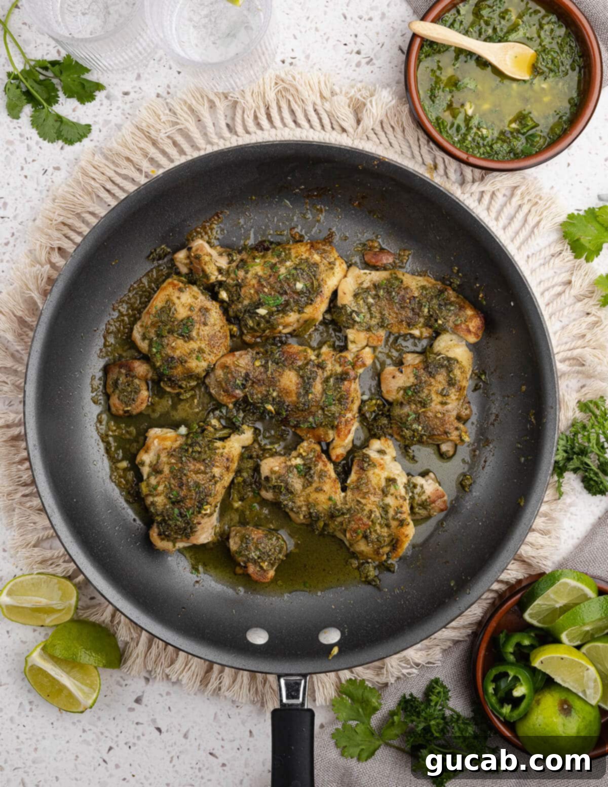 Zesty Chimichurri Chicken Thighs 11 Freshly baked chimichurri chicken thighs presented beautifully in a skillet, garnished with lime wedges and a small bowl of extra chimichurri, ready for serving.